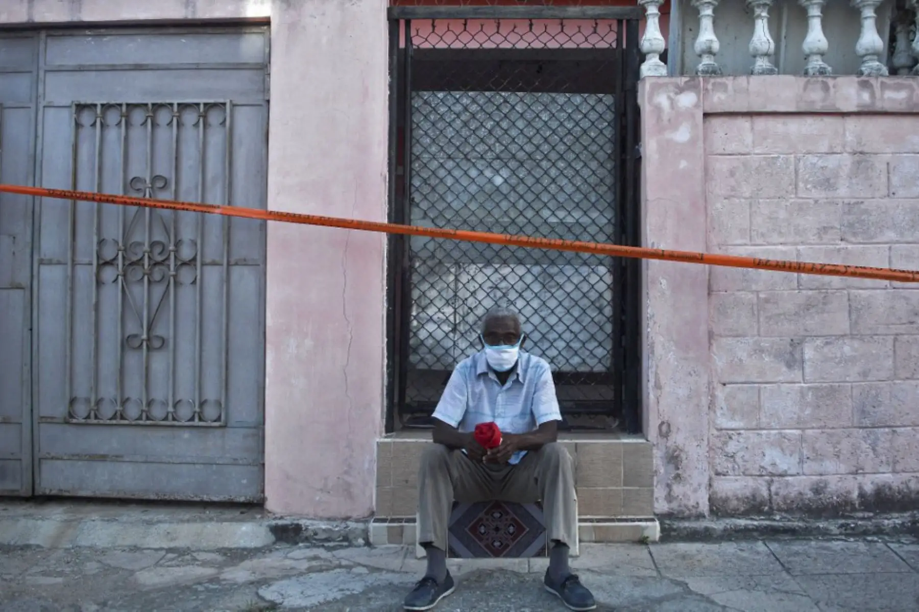 Un hombre se sienta en la puerta de su casa en un área acordonada luego de que se detectaran casos de covid-19 en La Habana. Cuba marcó un nuevo récord diario de casos positivos de covid-19 al confirmar 1183 infecciones en las últimas 24 horas. Foto: AFP
