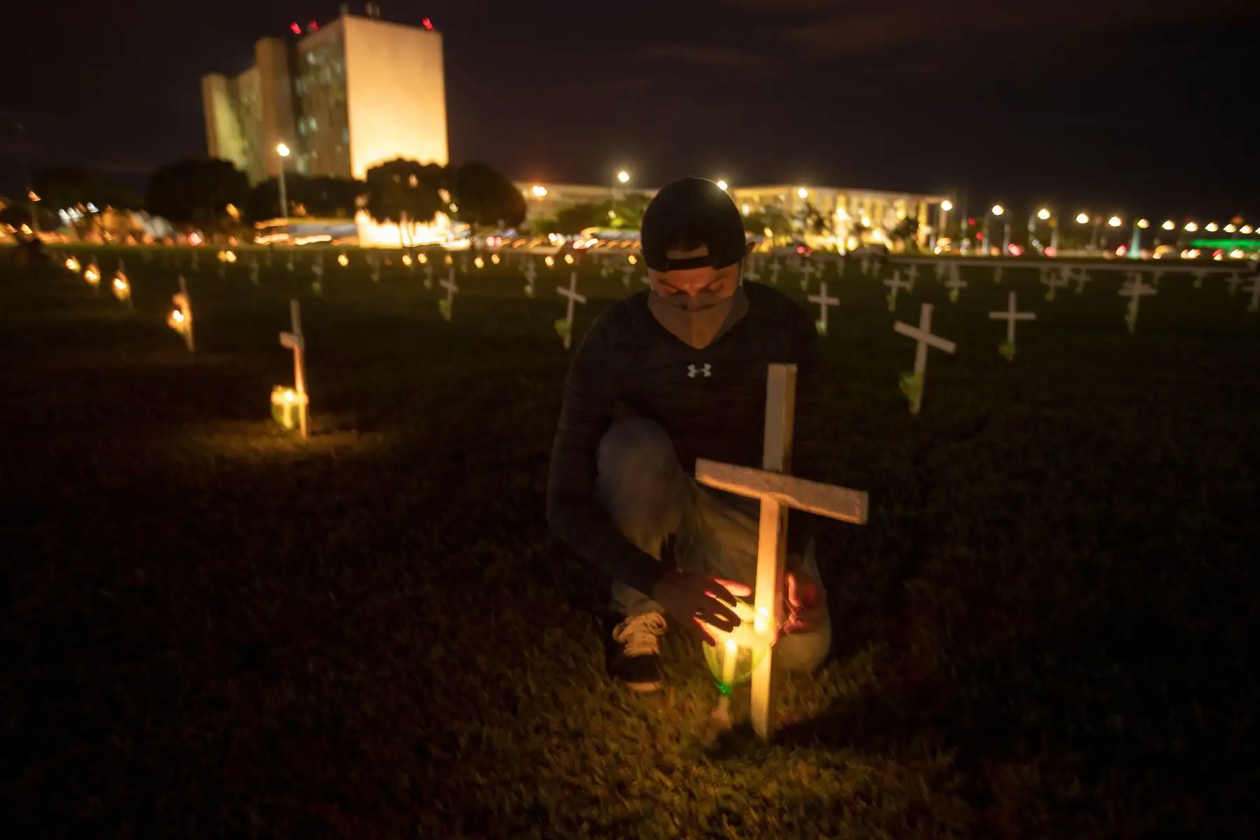 Un hombre enciende una vela junto a una cruz hoy 29 de abril del 2021 durante un homenaje a las víctimas mortales de la covid-19 hoy, en Brasilia. Foto: AFP