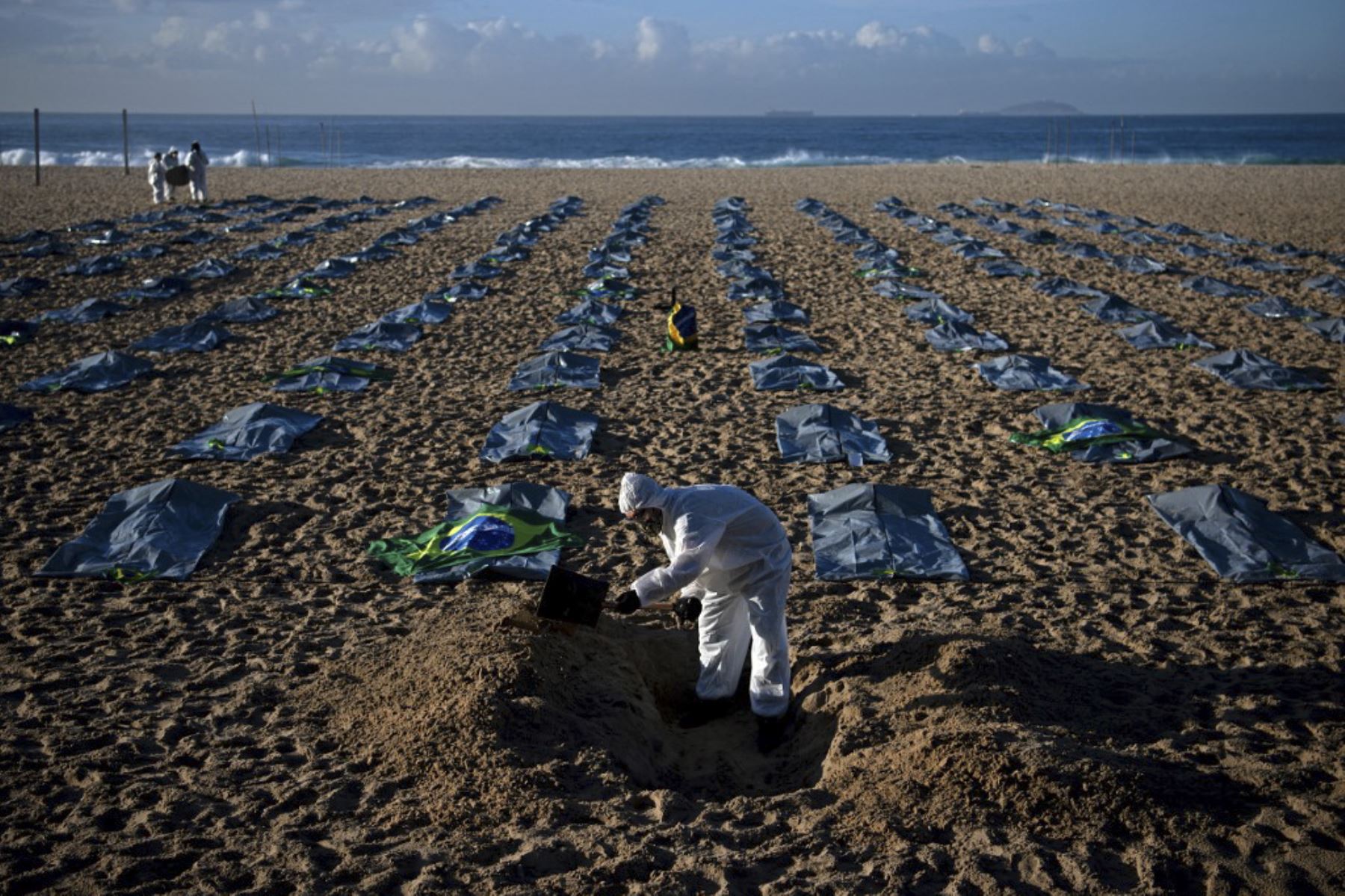 Un manifestante del grupo activista de derechos humanos de Río de Paz cava una tumba simbólica frente a filas de bolsas que simbolizan bolsas para cadáveres en la playa de Copacabana, durante una protesta contra el manejo del gobierno brasileño de la pandemia de coronavirus, en Río de Janeiro. Foto: AFP
