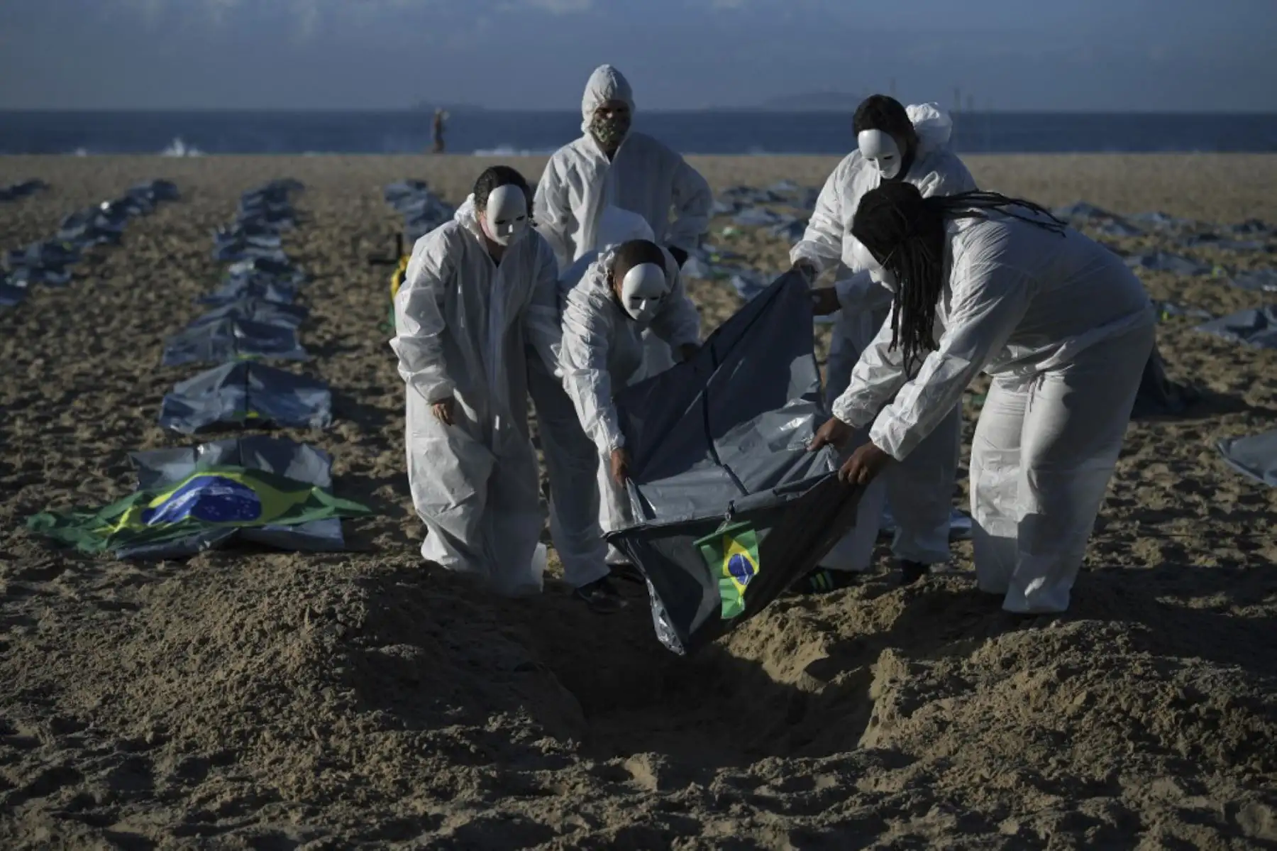 Manifestantes del grupo activista de derechos humanos de Río de Paz cavan una tumba simbólica frente a filas de bolsas que simbolizan bolsas para cadáveres en la playa de Copacabana, durante una protesta contra el manejo del gobierno brasileño de la pandemia de coronavirus, en Río de Janeiro. Foto: AFP