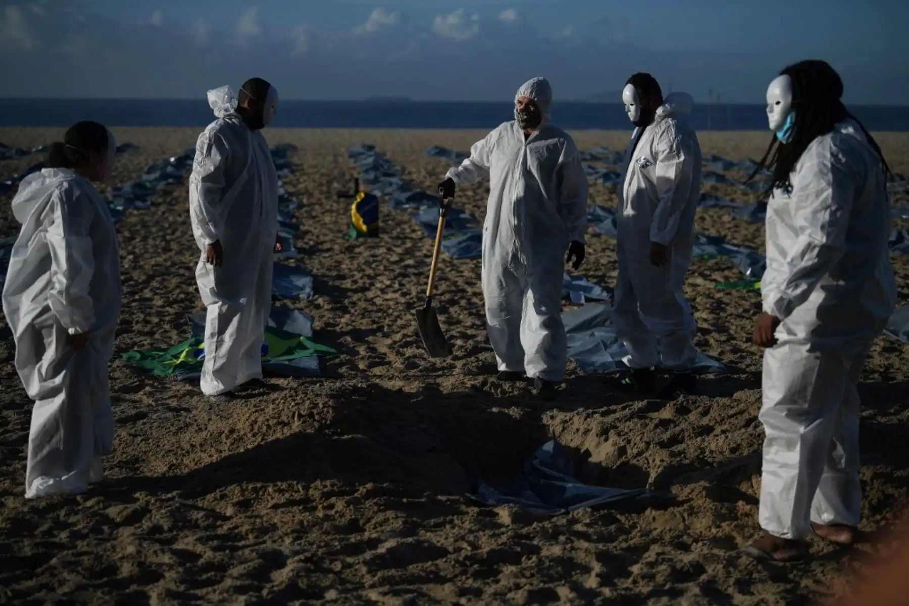 Manifestantes del grupo activista de derechos humanos de Río de Paz cavan una tumba simbólica frente a filas de bolsas que simbolizan bolsas para cadáveres en la playa de Copacabana, durante una protesta contra el manejo del gobierno brasileño de la pandemia de coronavirus, en Río de Janeiro. Foto: AFP