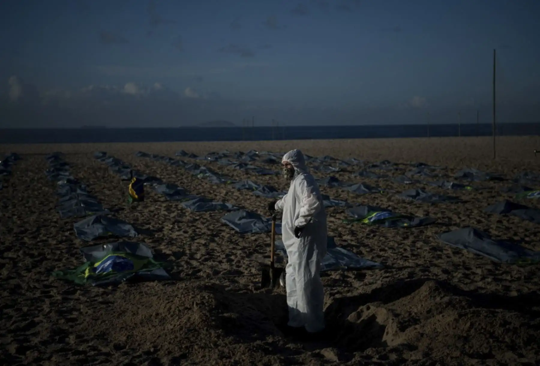 Un manifestante del grupo activista de derechos humanos de Río de Paz cava una tumba simbólica frente a filas de bolsas que simbolizan bolsas para cadáveres en la playa de Copacabana, durante una protesta contra el manejo del gobierno brasileño de la pandemia de coronavirus, en Río de Janeiro. Foto: AFP