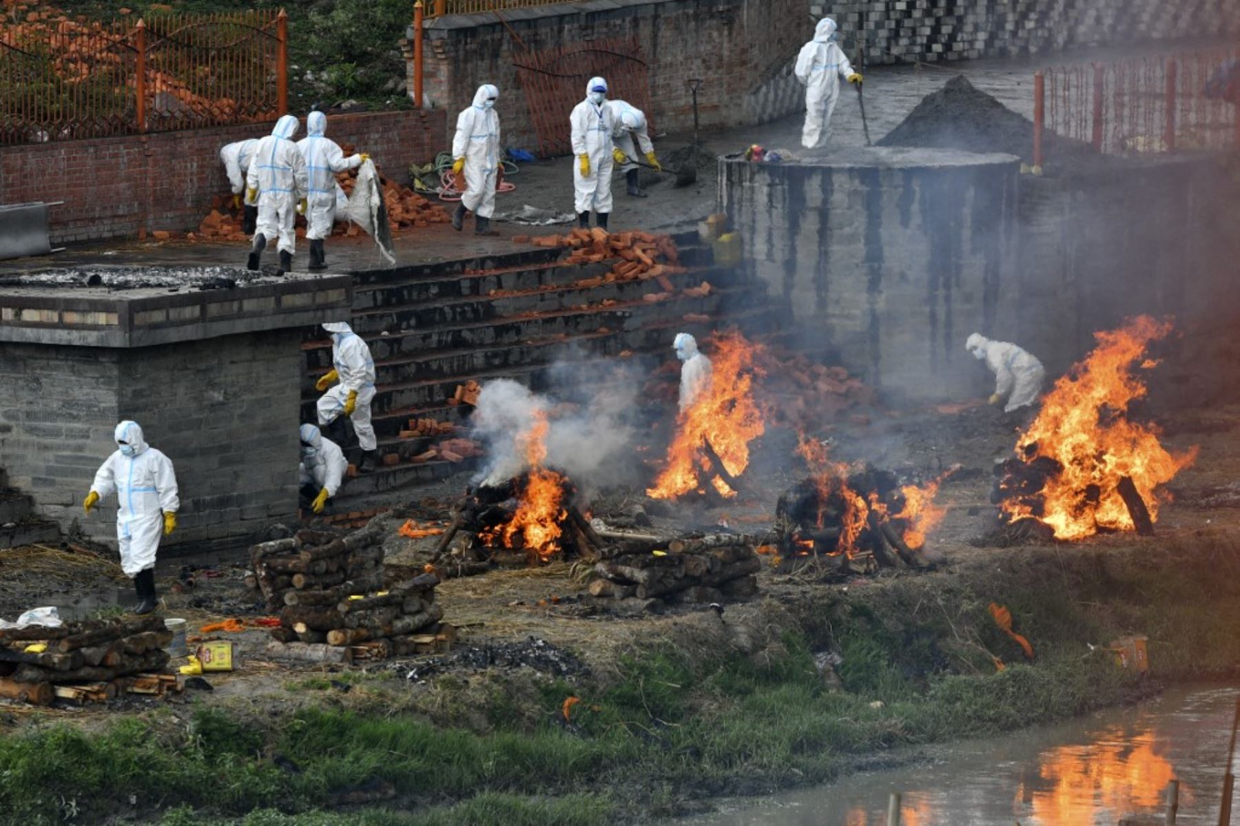 Los trabajadores que usan trajes de equipo de protección personal (PPE) extienden el área del crematorio junto a las piras funerarias de las personas que murieron debido a la enfermedad del coronavirus covid-19, en un crematorio en Katmandú. Foto: AFP