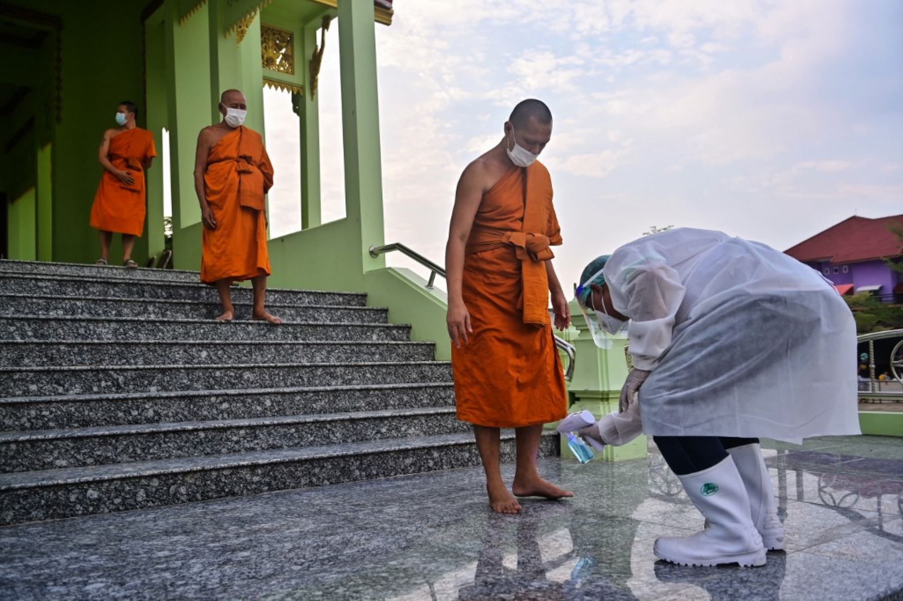Monjes budistas son rociados con desinfectante por voluntarios de rescate de la fundación Siam Nonthaburi después del funeral de una mujer que murió después de contraer el coronavirus covid-19 en el templo budista Wat Rat Prakhong Tham en Nonthaburi. Foto: AFP