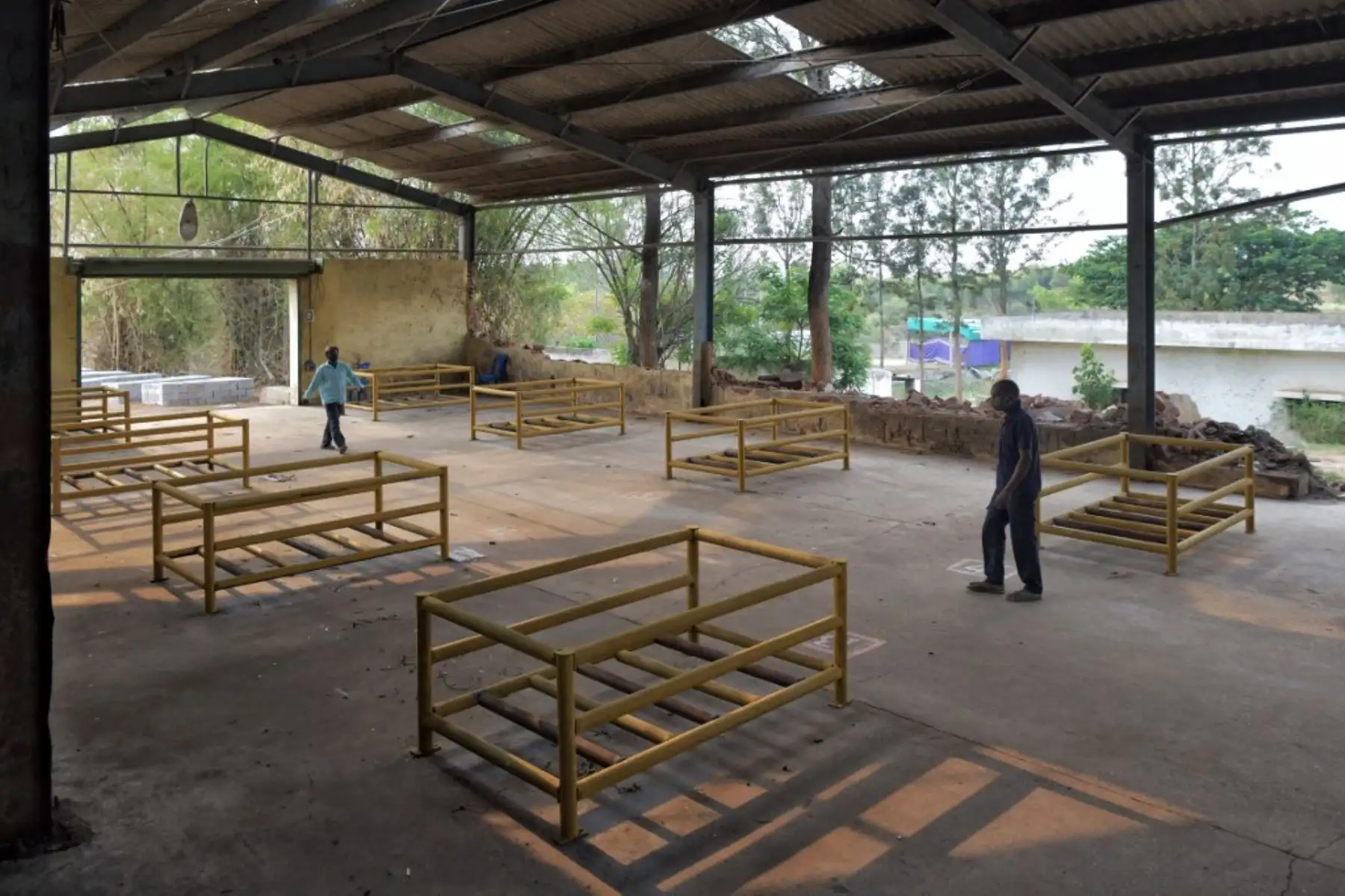 Los residentes locales caminan junto a los marcos de metal que se usarán para piras funerarias en el sitio propuesto por el gobierno de Karnantaka para un crematorio abierto para las víctimas del coronavirus covid-19, en la aldea de Mavallipura, donde los residentes se oponen a la ubicación del crematorio, en las afueras de Bangalore. Foto: AFP
