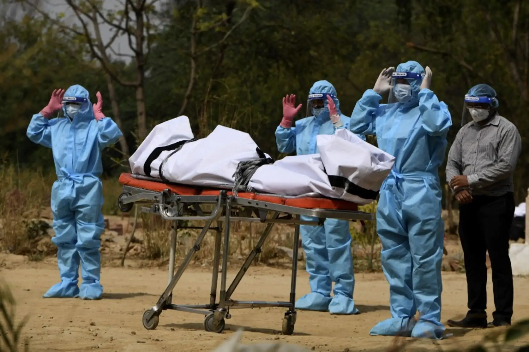 Familiares que usan equipo de protección personal (EPP) ofrecen oraciones fúnebres frente al cuerpo de una víctima del coronavirus covid-19 antes del entierro en un cementerio en Nueva Delhi el 30 de abril de 2021. Foto: AFP
