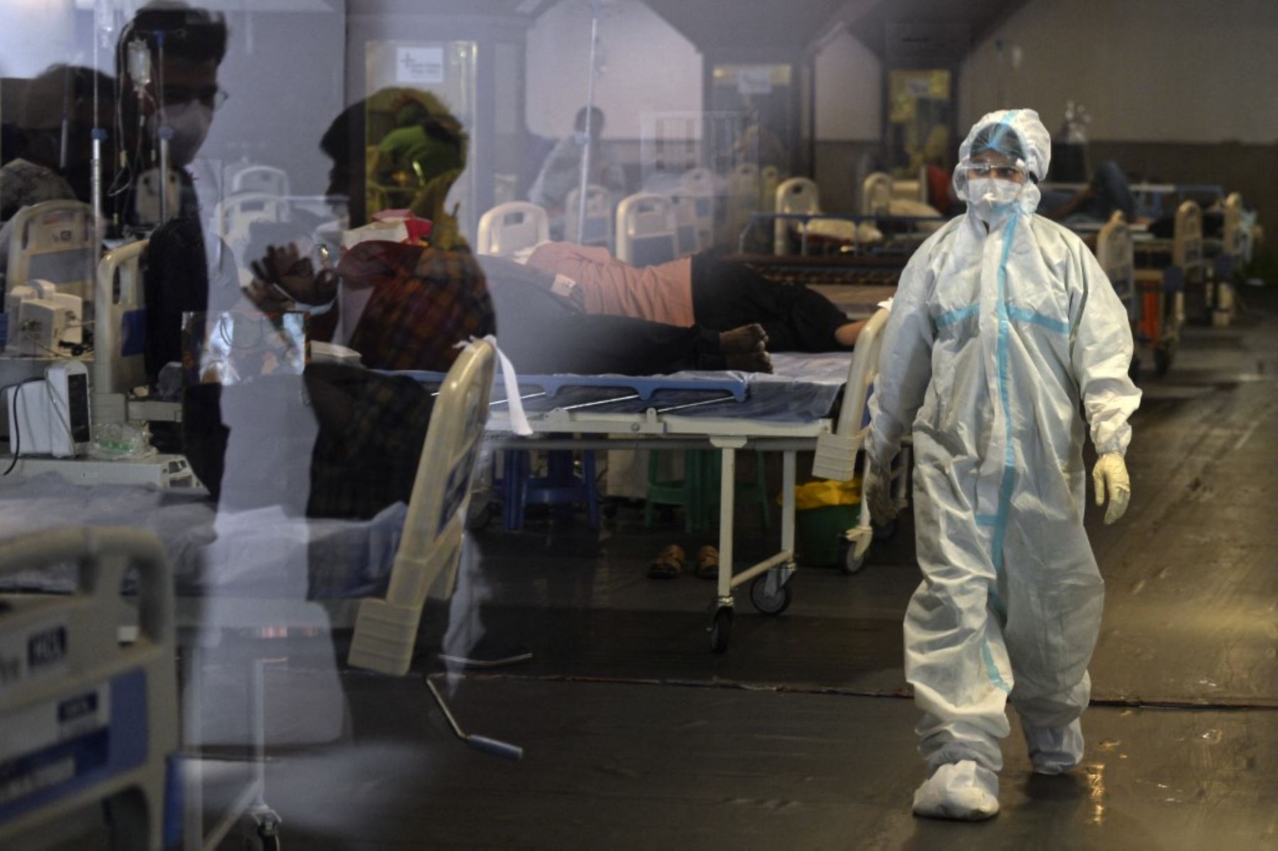 Un trabajador de la salud con un equipo de protección pasa junto a pacientes con coronavirus covid-19 dentro de un salón de banquetes convertido temporalmente en un centro de atención Covid en Nueva Delhi. Foto: AFP