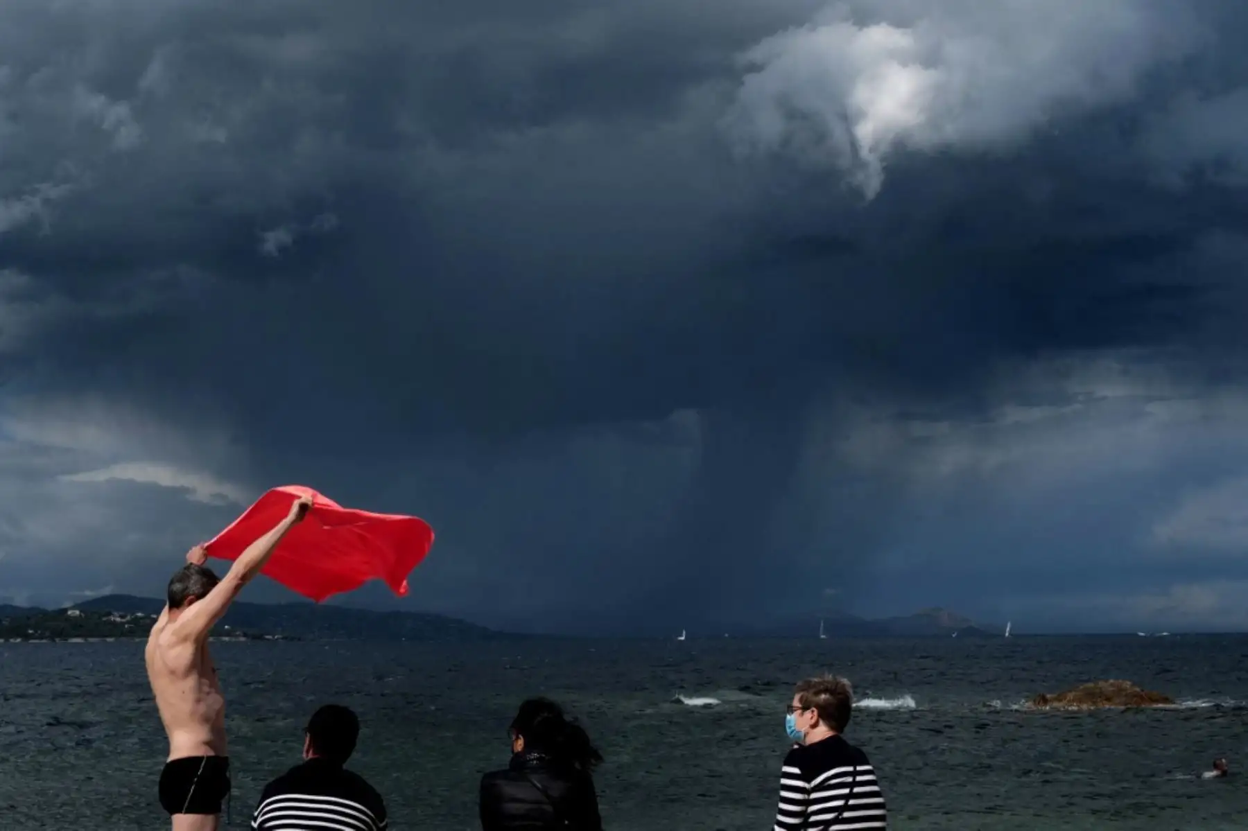 Un hombre retiene su toalla de playa debido al viento cuando se acerca una tormenta, en Saint-Tropez, en el sur de Francia. Foto: AFP