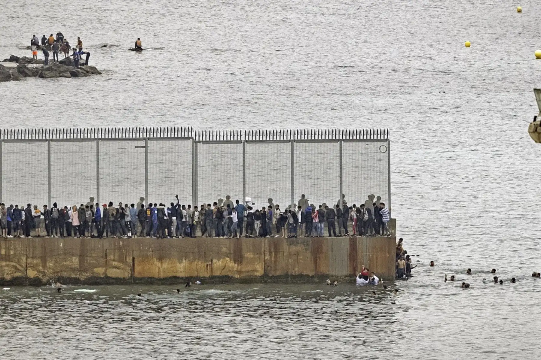 Migrantes marroquíes se reúnen junto a una valla fronteriza en la ciudad norteña de Fnideq en un intento de cruzar la frontera de Marruecos al enclave español de Ceuta, en el norte de África, el 18 de mayo de 2021. Foto: AFP
