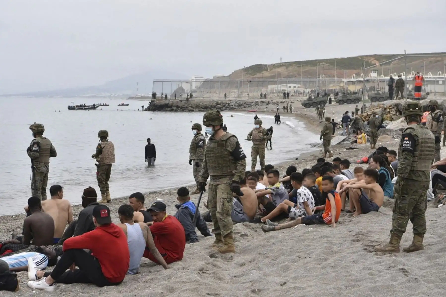 Los migrantes, incluidos los menores, que llegaron nadando al enclave español de Ceuta, descansan mientras los soldados españoles montan guardia el 18 de mayo de 2021 en Ceuta. España ha devuelto a Marruecos casi la mitad de los 6.000 migrantes que entraron en su enclave de Ceuta, mientras cientos más intentaban entrar en su otro territorio del norte de África. Foto: AFP