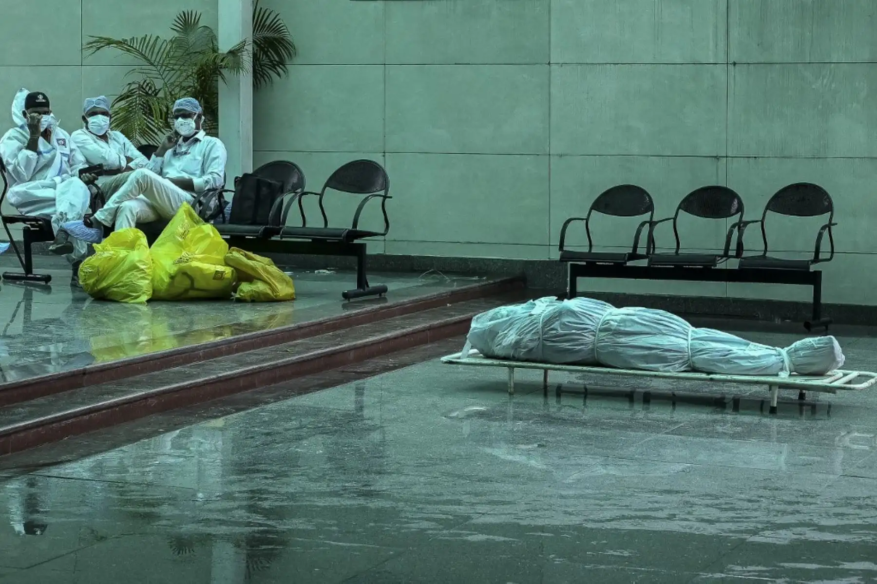 Trabajadores de la salud con trajes de Equipo de Protección Personal (EPP) se sientan junto al cadáver de una persona que murió debido al coronavirus Covid-19, en un crematorio en Nueva Delhi el 19 de mayo de 2021. Foto: AFP