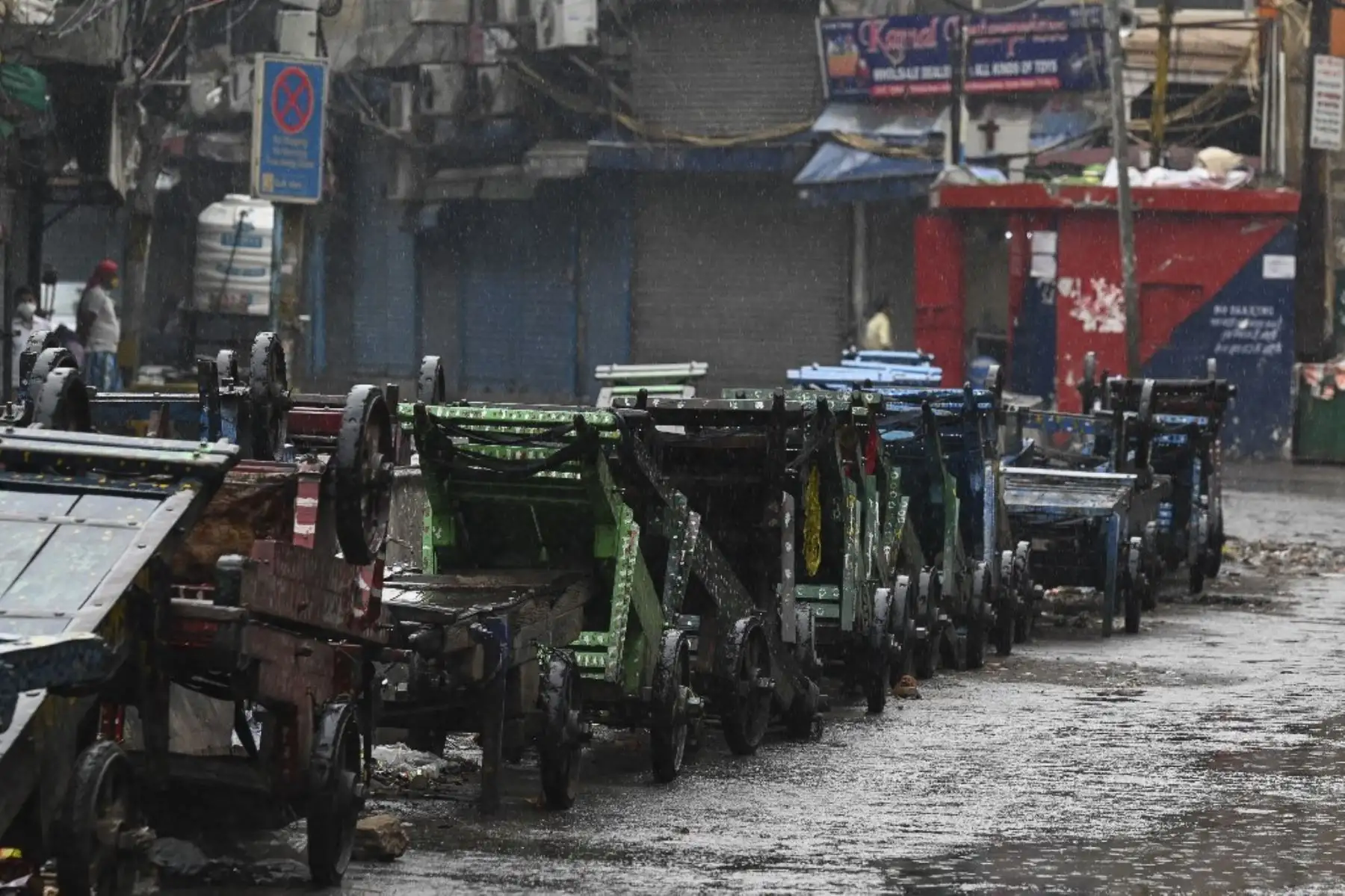 Un trabajador se sienta frente a tiendas cerradas mientras llueve durante un encierro impuesto como medida preventiva contra el coronavirus Covid-19, en Nueva Delhi el 19 de mayo de 2021. Foto: AFP