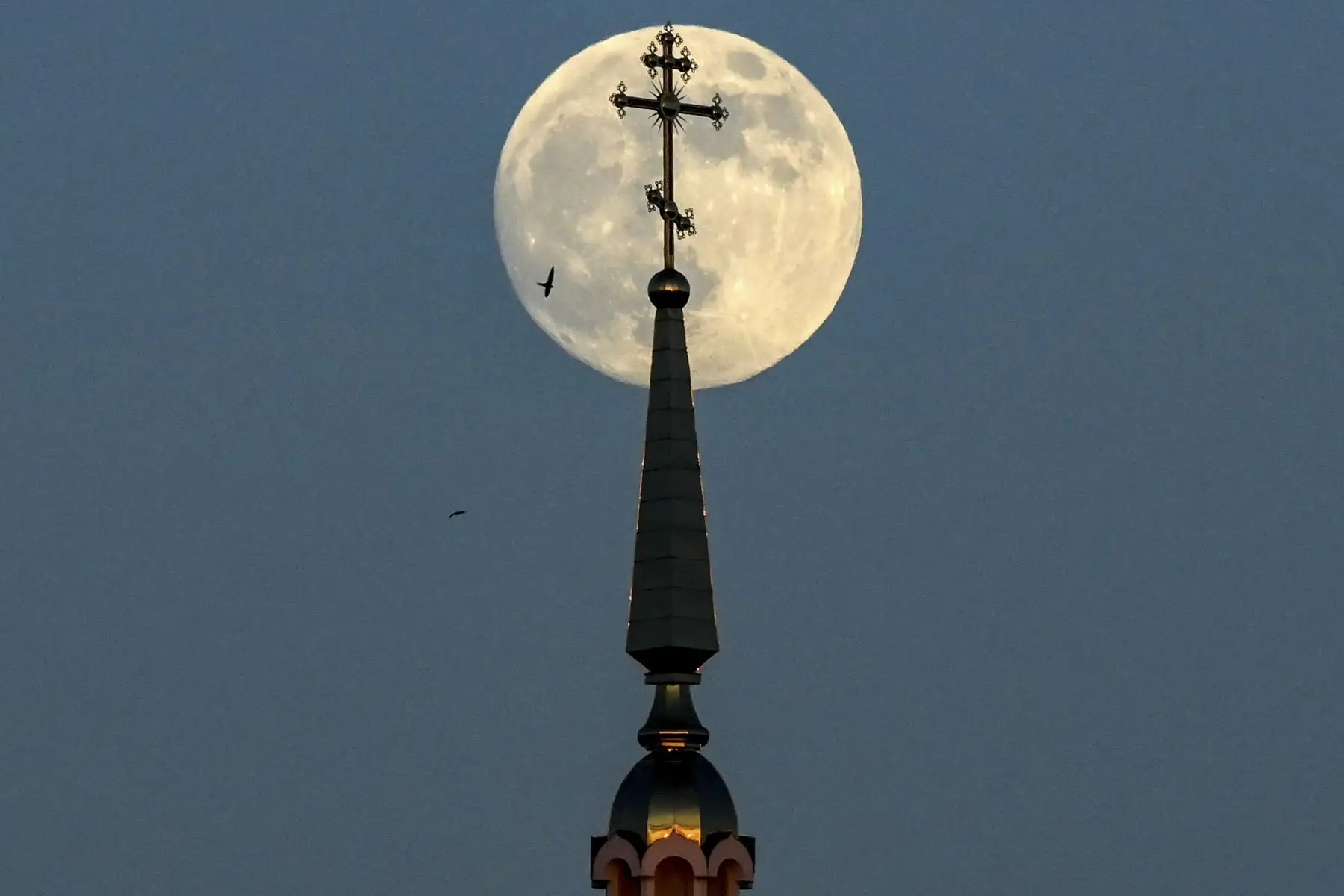 La luna llena se muestra detrás de una cruz en la parte superior de una iglesia ortodoxa en la ciudad de Rossosh 