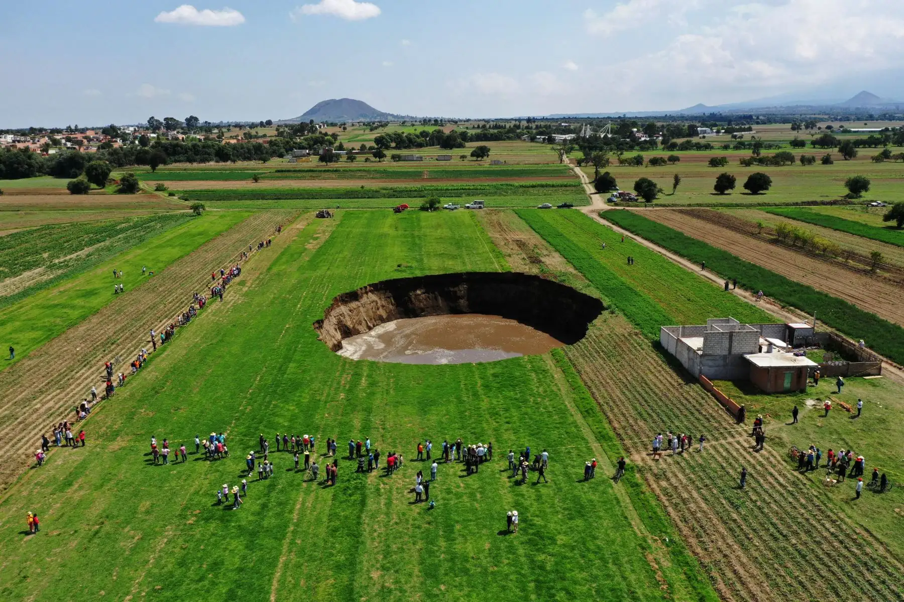 La familia Sánchez descubrieron que a unos metros de su casa, en medio del campo, la tierra se había hundido.
El socavón está relleno de agua, rodeado por campos verdes y acordonado por las autoridades.
Foto: AFP