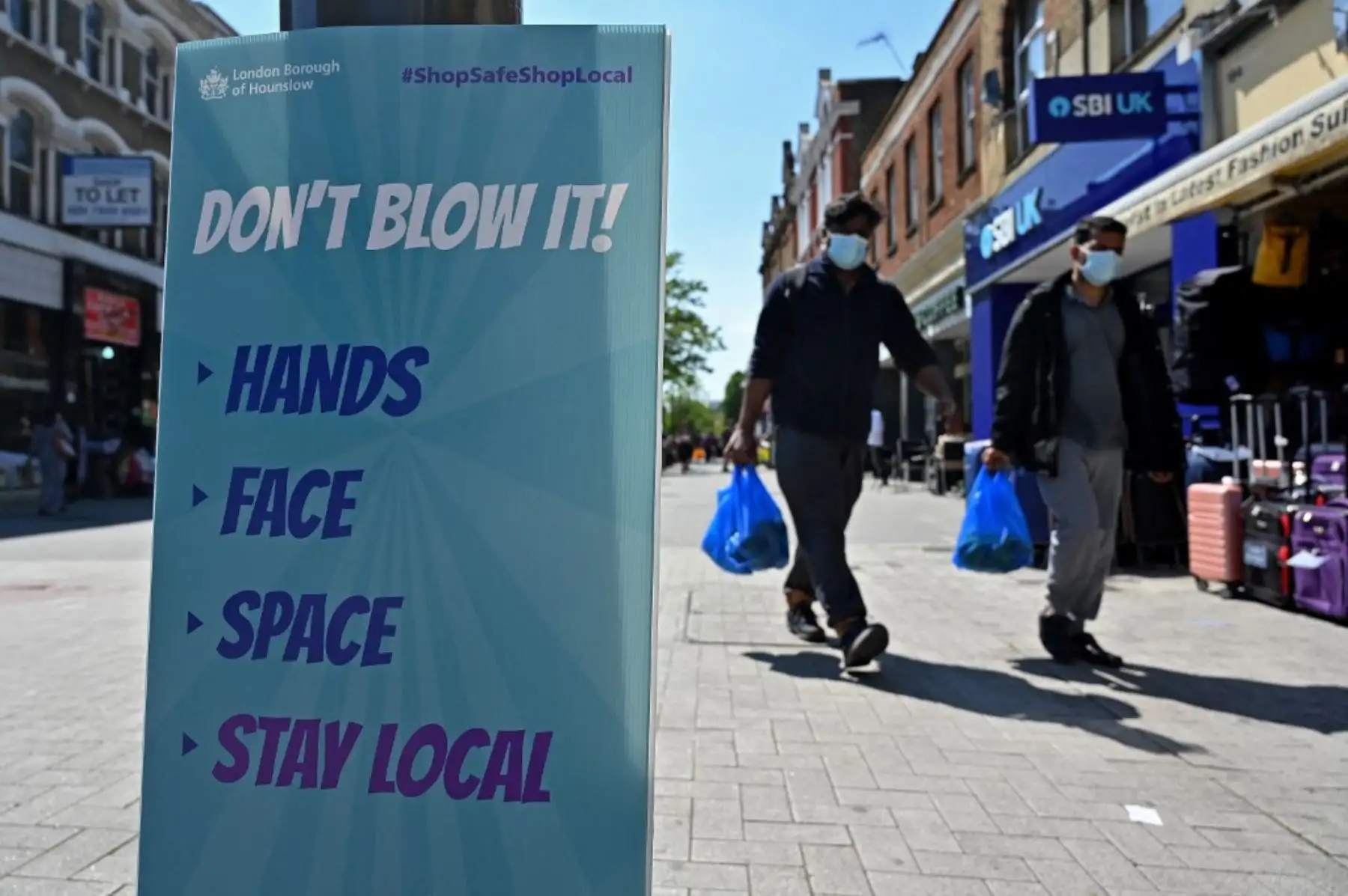 Los peatones pasan junto a un letrero que advierte al público sobre la propagación del coronavirus mientras caminan por la calle en Hounslow, al oeste de Londres. Foto: AFP