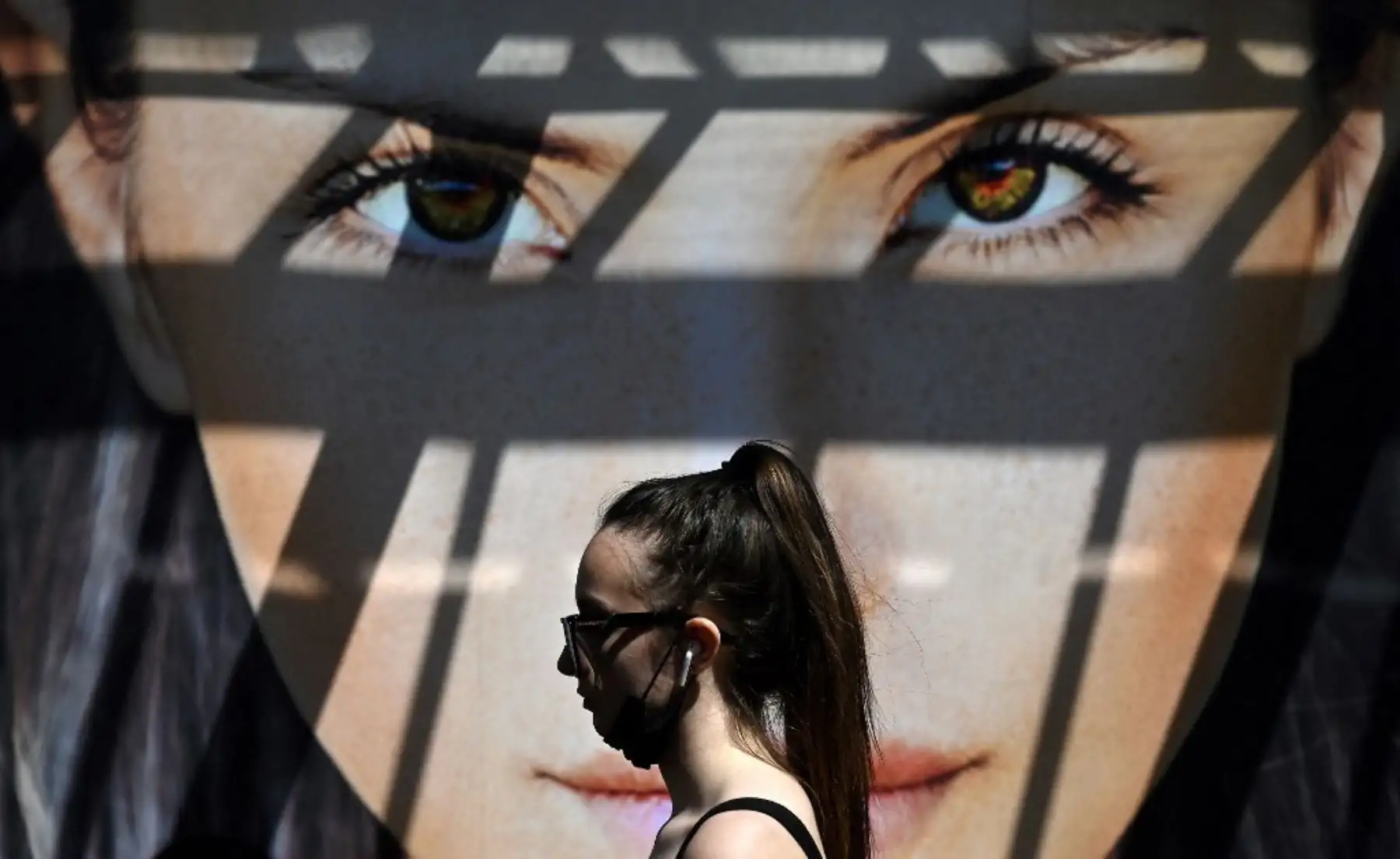 Un peatón con una cubierta facial debido a Covid-19, pasa junto a una imagen en una valla publicitaria en Hounslow, en el oeste de Londres. Foto: AFP