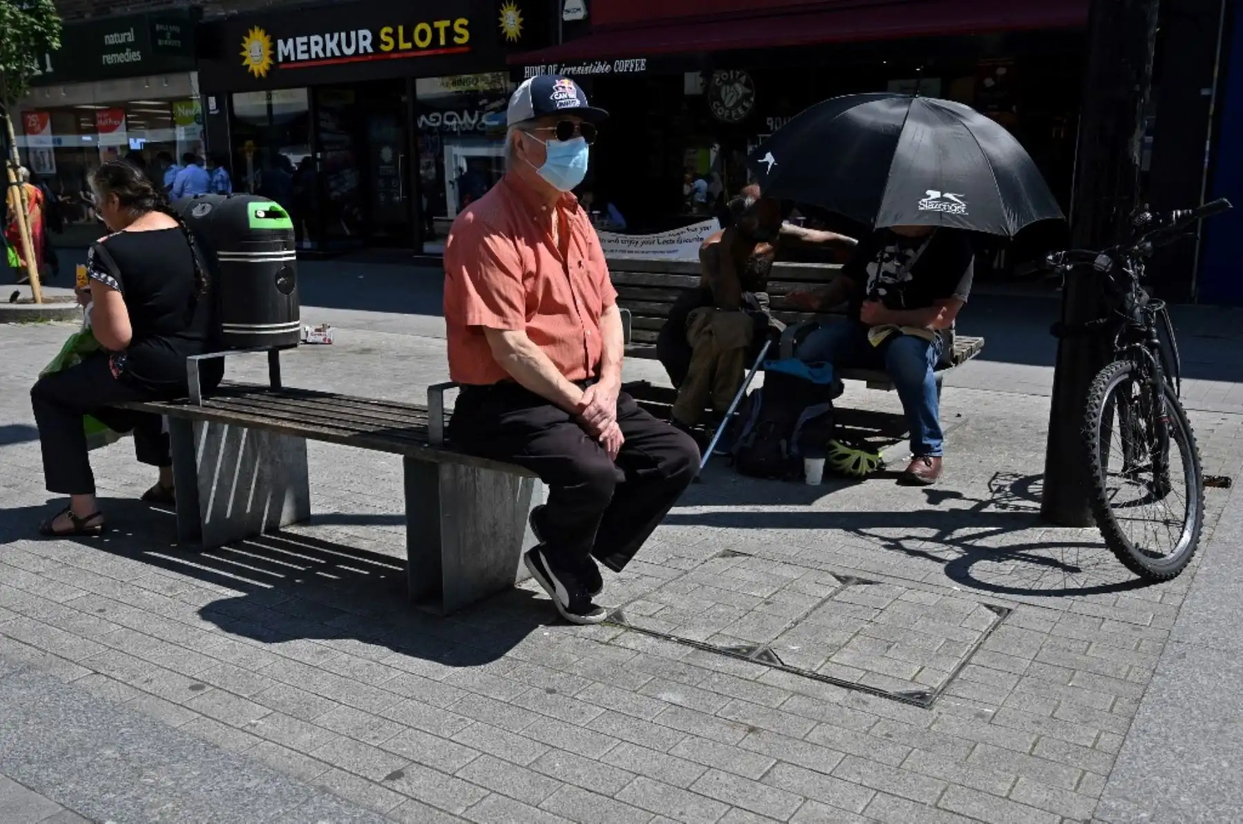 Un hombre que usa mascarilla para protegerse del covid-19, se sienta fuera de las tiendas en Hounslow, al oeste de Londres. Foto: AFP