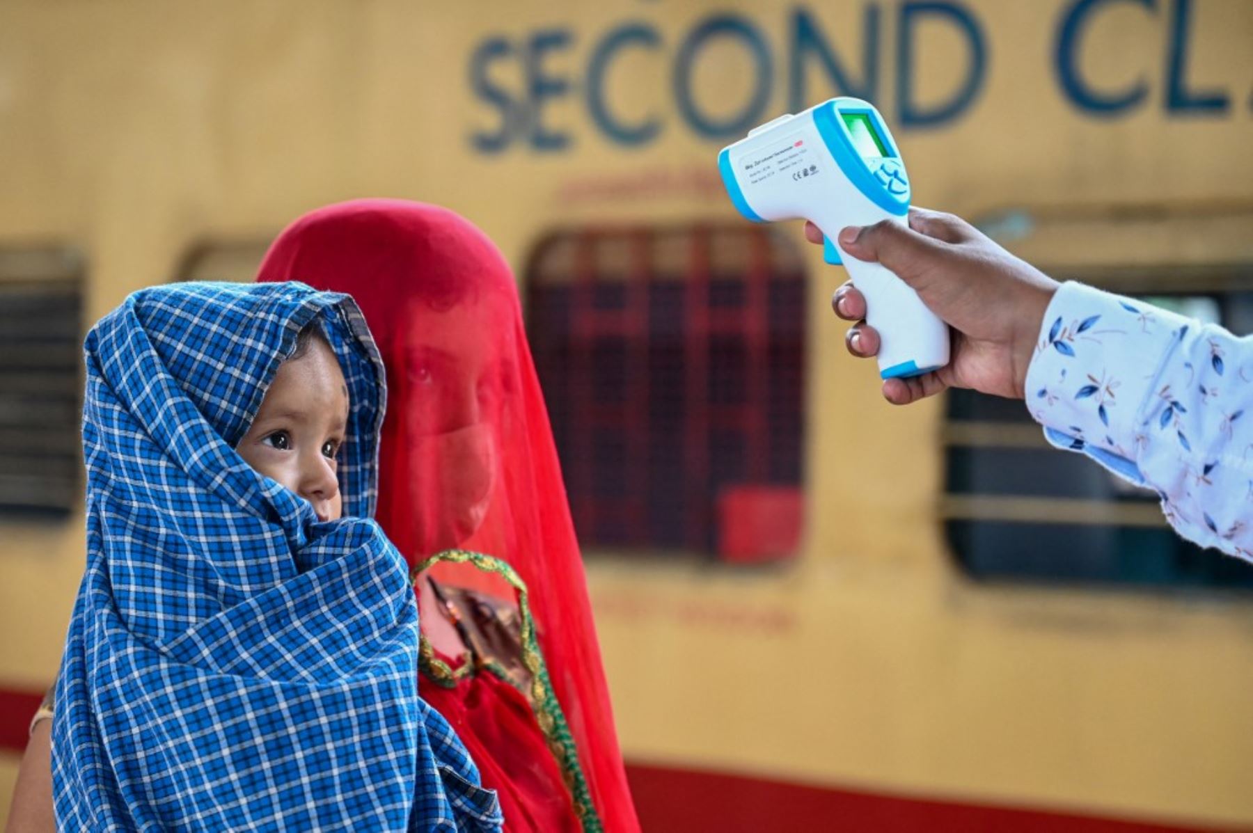 Un trabajador de la salud controla la temperatura corporal de un pasajero durante una prueba de detección del coronavirus Covid-19 cuando llega con su hijo a una plataforma ferroviaria en un tren de larga distancia, en Mumbai el 8 de junio de 2021. Foto: AFP