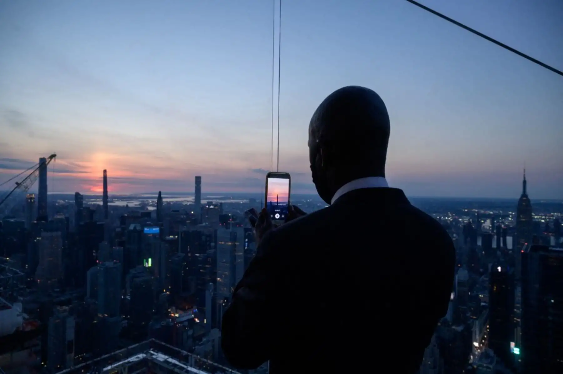 Un hombre que sostiene un teléfono móvil se encuentra frente al horizonte de Manhattan mientras espera el inicio del eclipse solar parcial, en el mirador de Edge, en Nueva York el 10 de junio de 2021. Foto: AFP