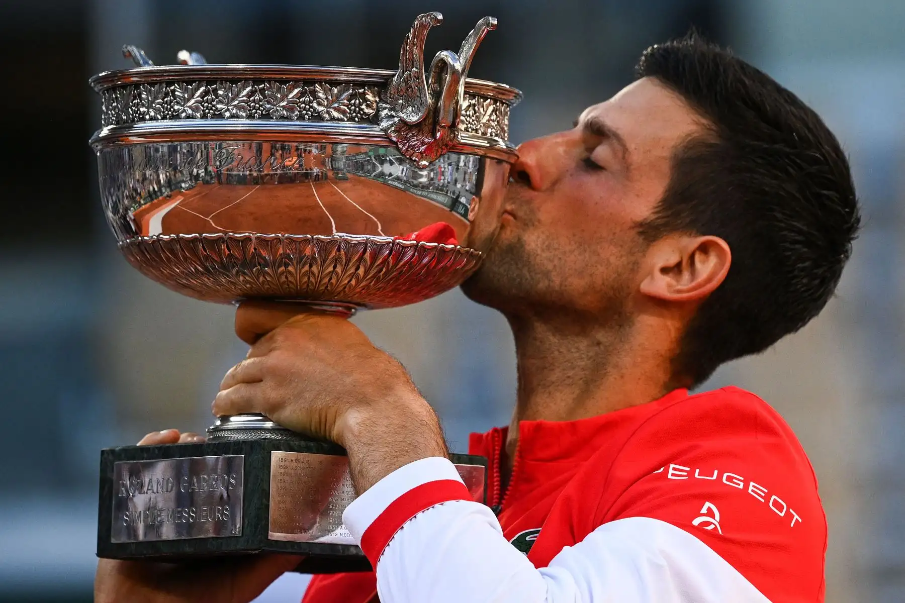El serbio Novak Djokovic besa la Copa Mousquetaires  mientras celebra después de ganar al griego Stefanos Tsitsipas al final de su último partido de tenis masculino el día 15 del torneo de tenis Roland Garros 2021 del Abierto de Francia en París.
Foto: AFP