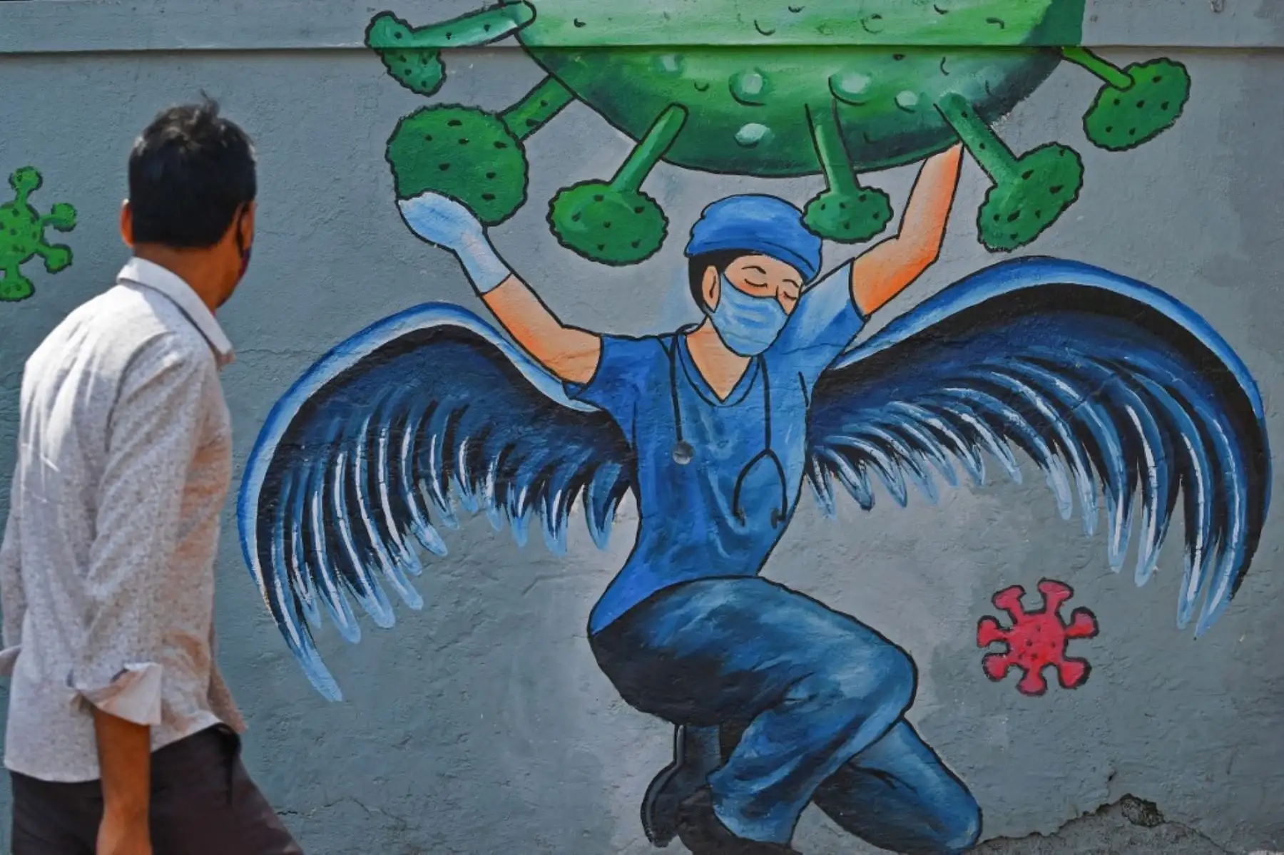 Un peatón pasa junto a un mural que representa medidas de concientización contra el coronavirus Covid-19 que presenta a un personal médico de primera línea como ángel de la guarda, en Navi Mumbai. Foto: AFP
