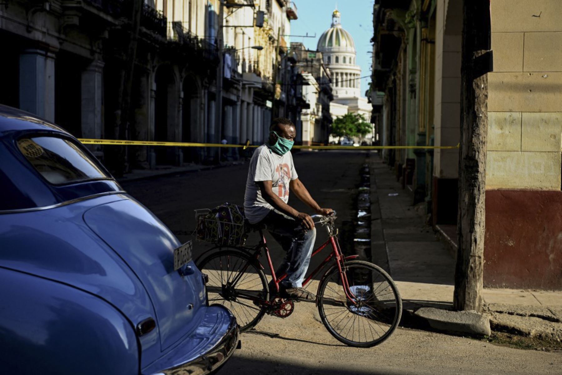Un hombre con máscara facial pasa en bicicleta por un área restringida debido a casos positivos de covid-19 en La Habana, Cuba. Foto: AFP