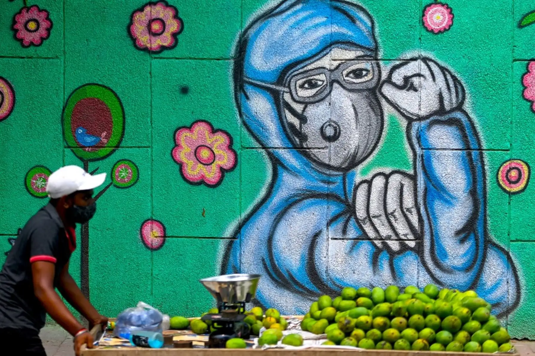 Un vendedor de frutas tira de su carrito mientras pasa junto a un mural que muestra a un trabajador del coronavirus Covid-19 de primera línea con una máscara facial en Nueva Delhi. Foto: AFP