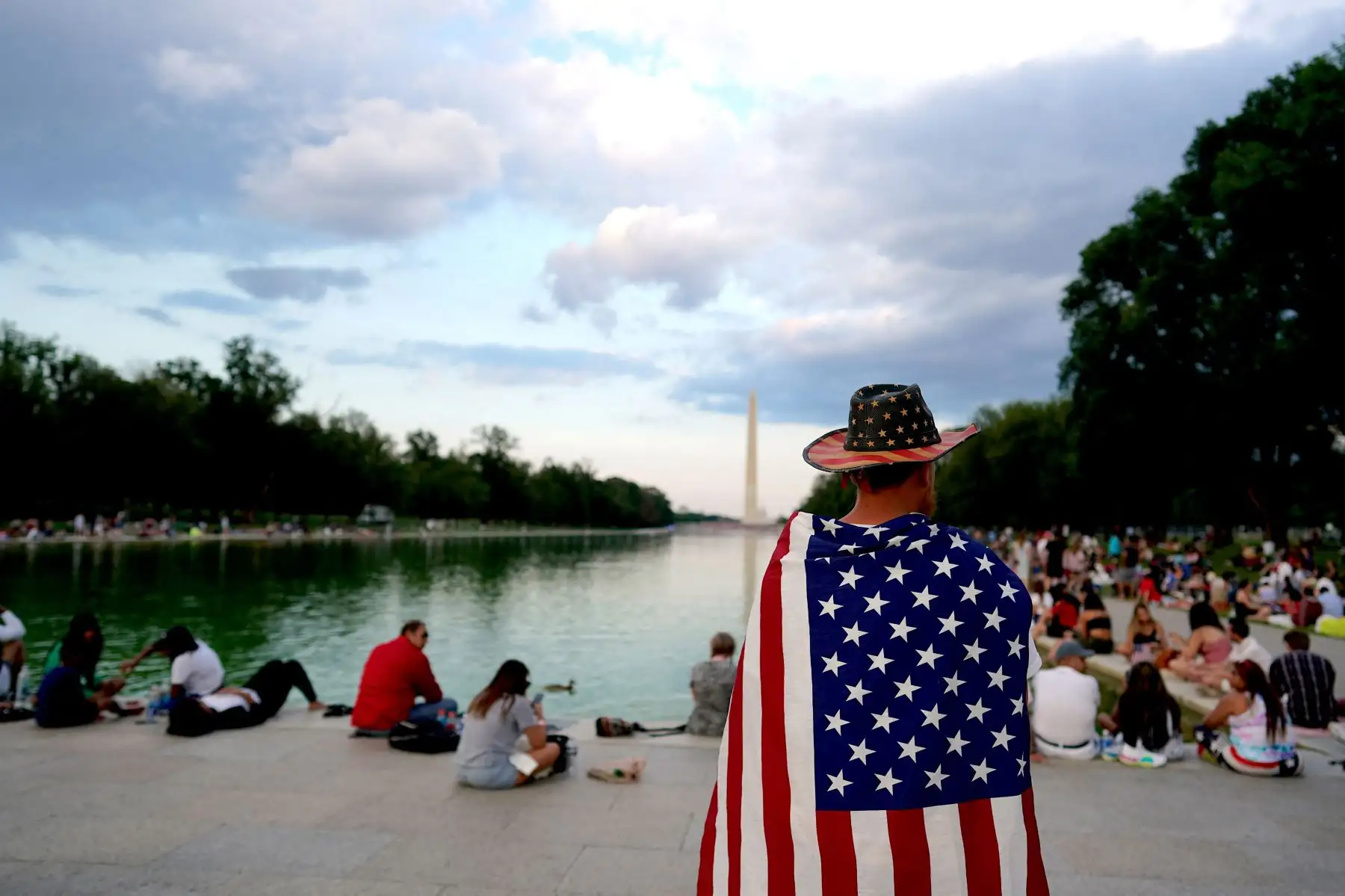 Una persona lleva una bandera de los EE. UU. sobre sus hombros cuando los visitantes llegan antes de ver la exhibición de fuegos artificiales del Día de la Independencia cerca del Monumento a Lincoln en el National Mall el 4 de julio de 2021 en Washington, DC. Foto: AFP