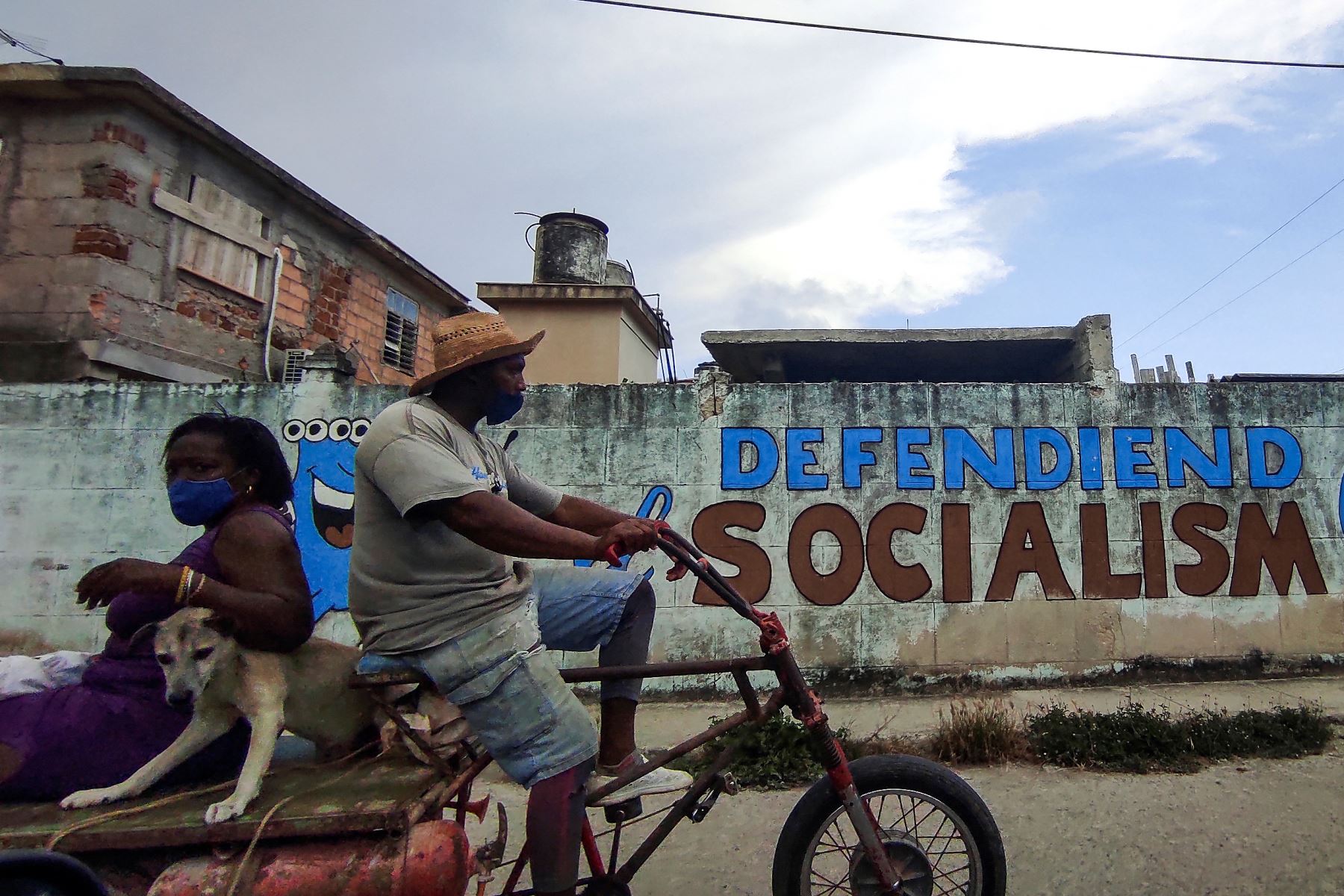 La gente monta un triciclo cerca de un graffiti que dice:  Defendiendo el socialismo en La Habana. Foto: AFP