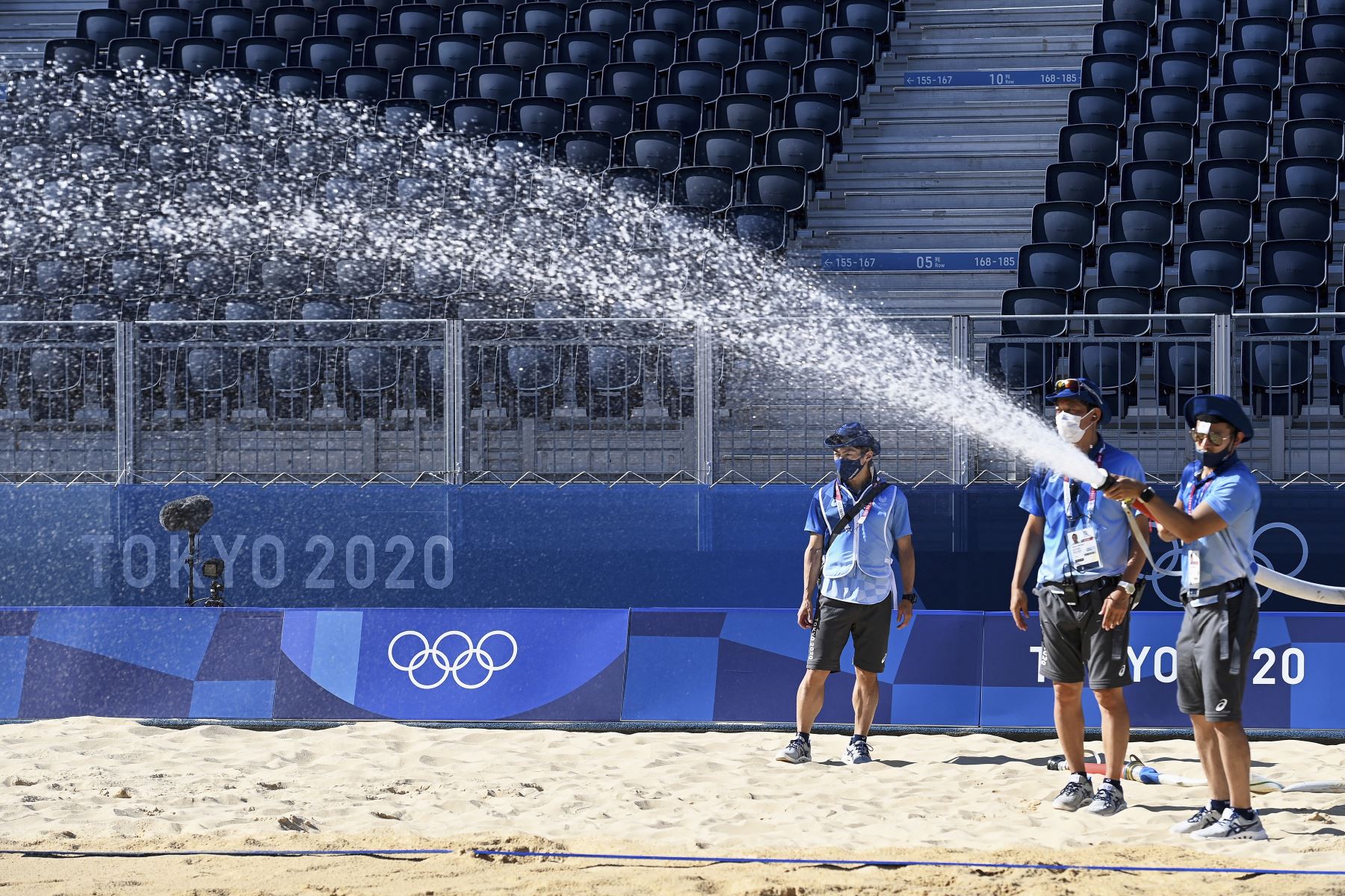 Los trabajadores rocían agua en la cancha olímpica de voleibol de playa durante una sesión de entrenamiento en el parque Shiokaze en Tokio. Foto: AFP