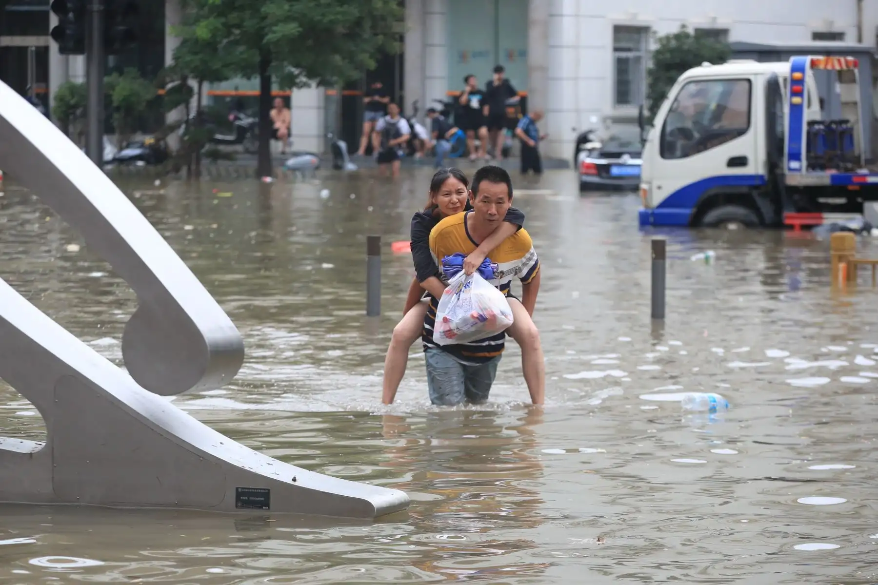 Un hombre carga a una mujer para cruzar la carretera  completamente inundada, en la ciudad de Zhengzhou, en la provincia de Henan, en el centro de China. Foto: EFE