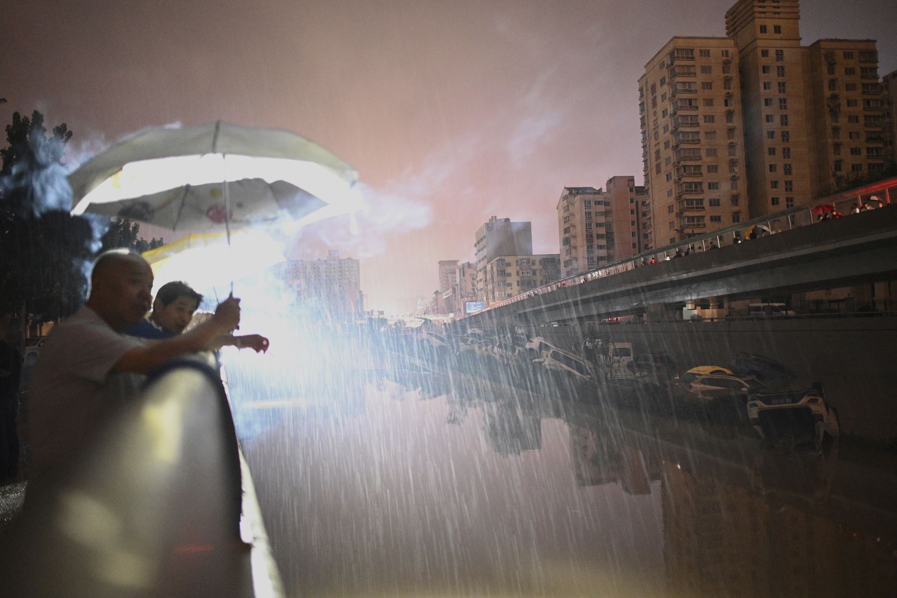 La gente mira los autos sumergidos en la vía tras las fuertes lluvias en Zhengzhou, en la provincia de Henan, en China. Foto: AFP
