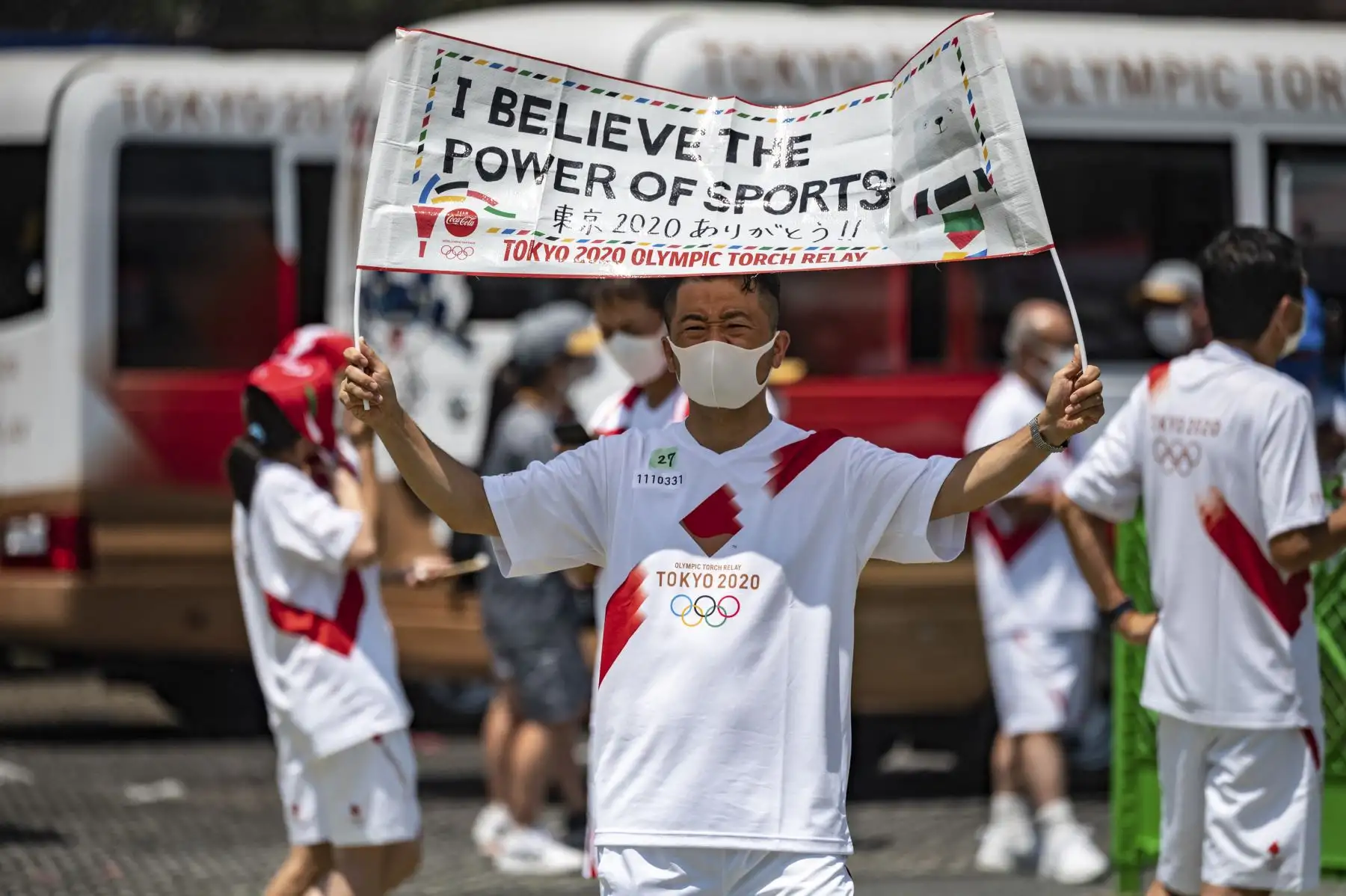 El portador de la antorcha Akimasa Sano sostiene una pancarta que dice "Creo en el poder de los deportes" durante la ceremonia de iluminación en el parque Hamacho en el distrito de Nihonbashi de Tokio. Foto: AFP