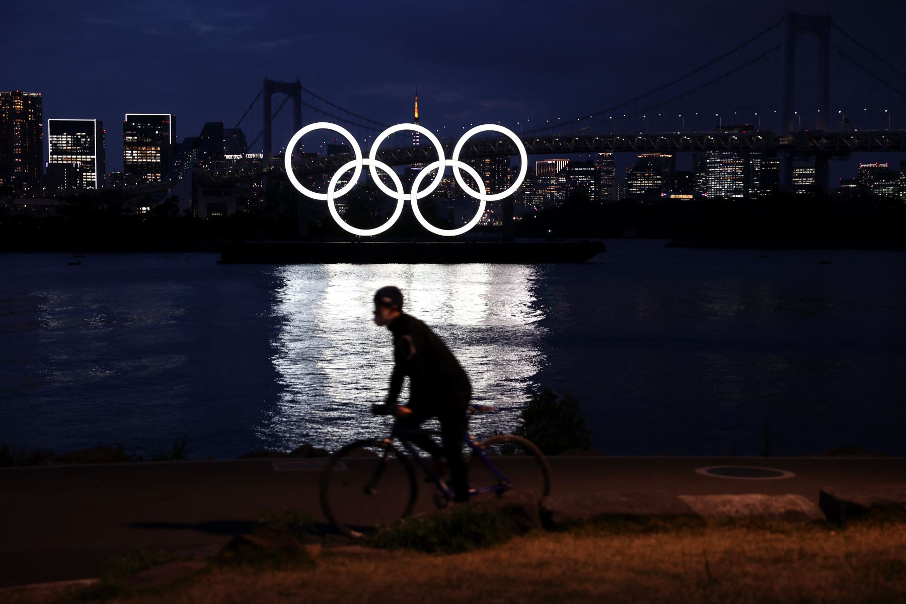 Un hombre monta su bicicleta frente a los anillos olímpicos en el paseo marítimo de Odaiba en Tokio. Foto: AFP