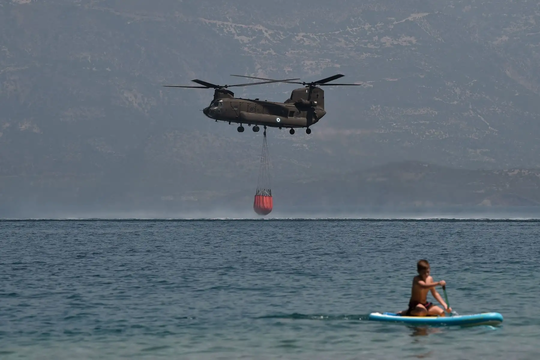 Un helicóptero Ch-47D Chinook es observado por un bañista mientras se llena de agua para apagar incendios cerca de la playa Lambiri en Patras.
Foto : AFP