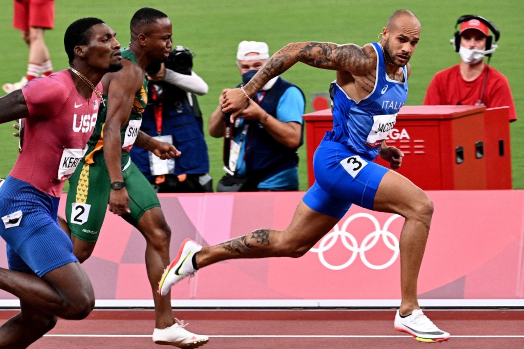El italiano Lamont Marcell Jacobs, el sudafricano Akani Simbine y el estadounidense Fred Kerley compiten en la final masculina de los 100 metros durante los Juegos Olímpicos de Tokio 2020.

Foto: AFP