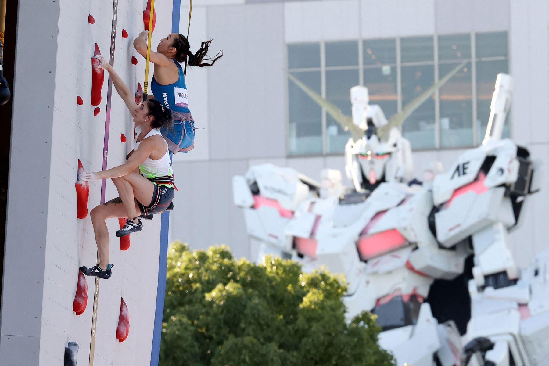 La japonesa Akiyo Noguchi  y la eslovena Mia Krampl compiten en la calificación de velocidad de escalada deportiva femenina mientras que el robot de tamaño real de la animación japonesa, 