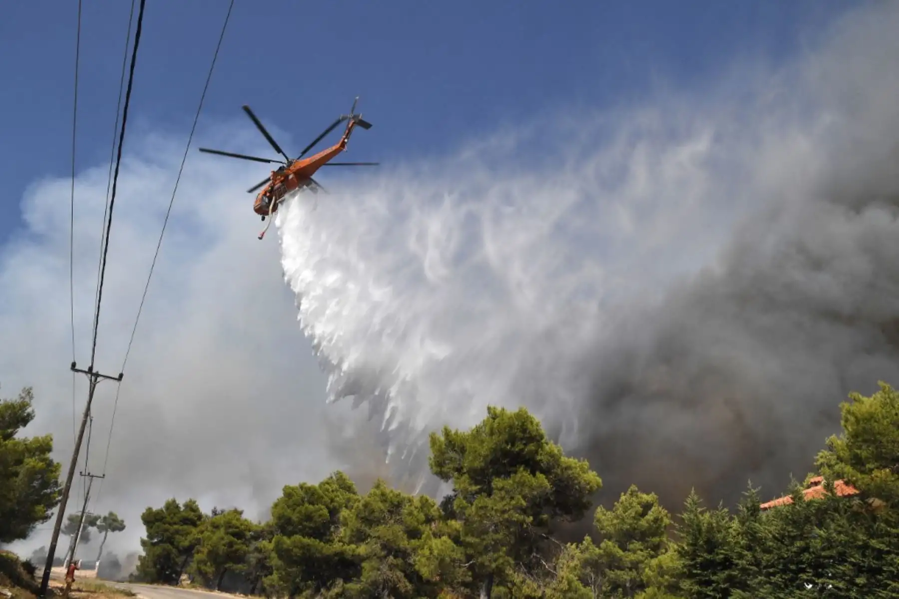 Un helicóptero vierte agua mientras un incendio se propaga cerca de las casas en Ippokratios Politia, a unos 30 kilómetros al norte de Atenas, el 6 de agosto de 2021. - Cientos de bomberos combatieron un incendio en las afueras de Atenas el 6 de agosto mientras decenas de incendios se desataban en Grecia. Foto: AFP