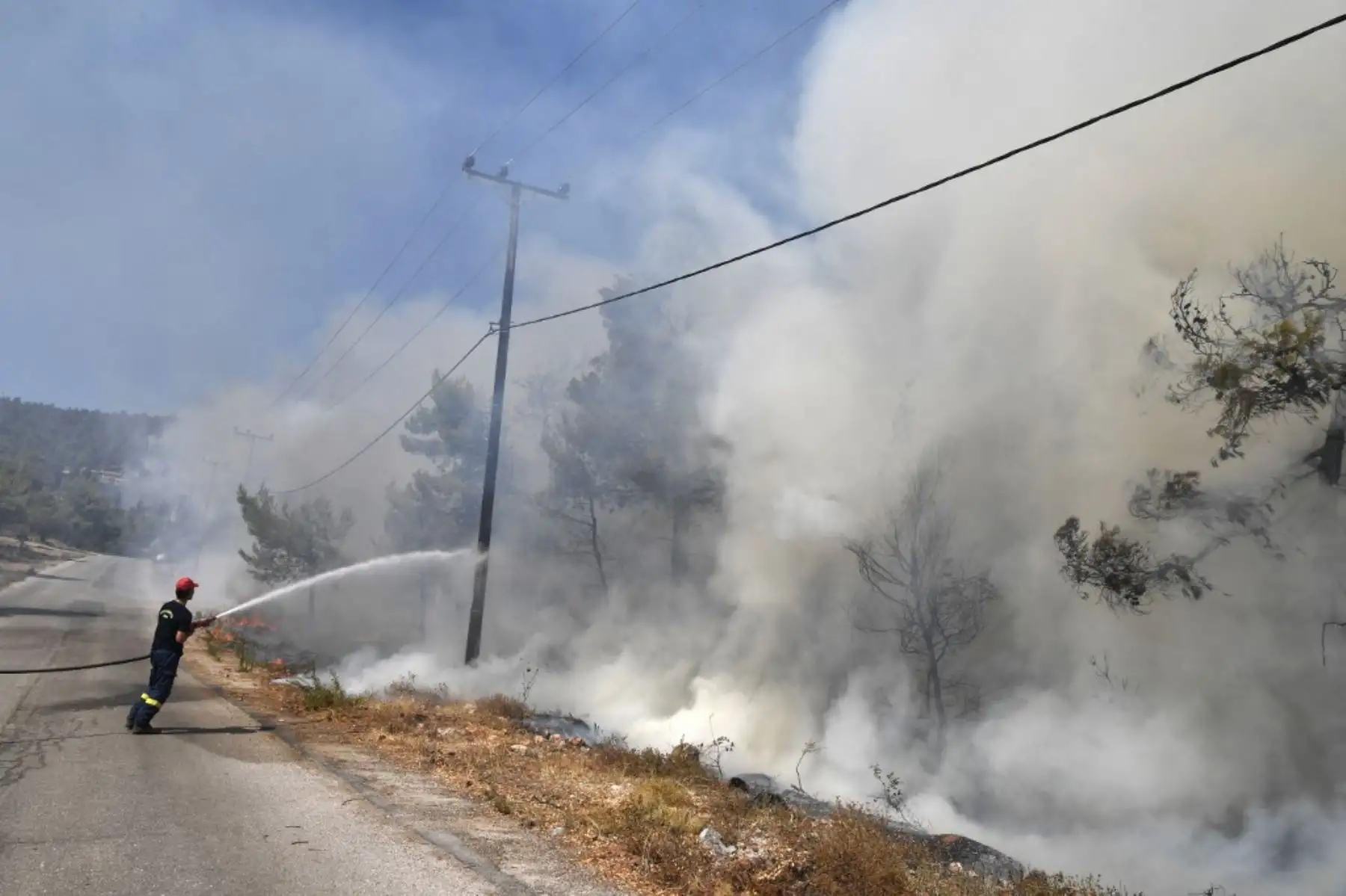 Un bombero rocía agua mientras un incendio se propaga cerca de las casas en Ippokratios Politia, a unos 30 kilómetros al norte de Atenas, el 6 de agosto de 2021. - Cientos de bomberos combatieron un incendio en las afueras de Atenas el 6 de agosto mientras decenas de incendios se desataban en Grecia. Foto: AFP