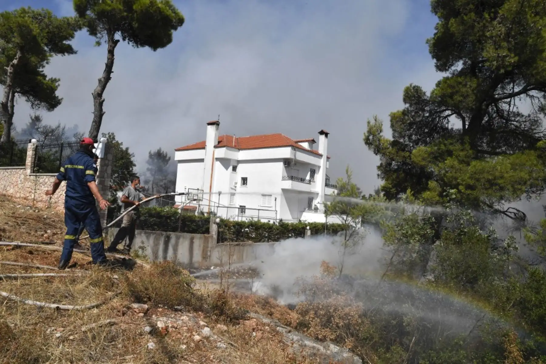 Un residente local rocía agua mientras un incendio se propaga cerca de las casas en Ippokratios Politia, a unos 30 kilómetros al norte de Atenas, el 6 de agosto de 2021. - Cientos de bomberos combatieron un incendio en las afueras de Atenas el 6 de agosto mientras decenas de incendios se desataban en Grecia. Foto: AFP