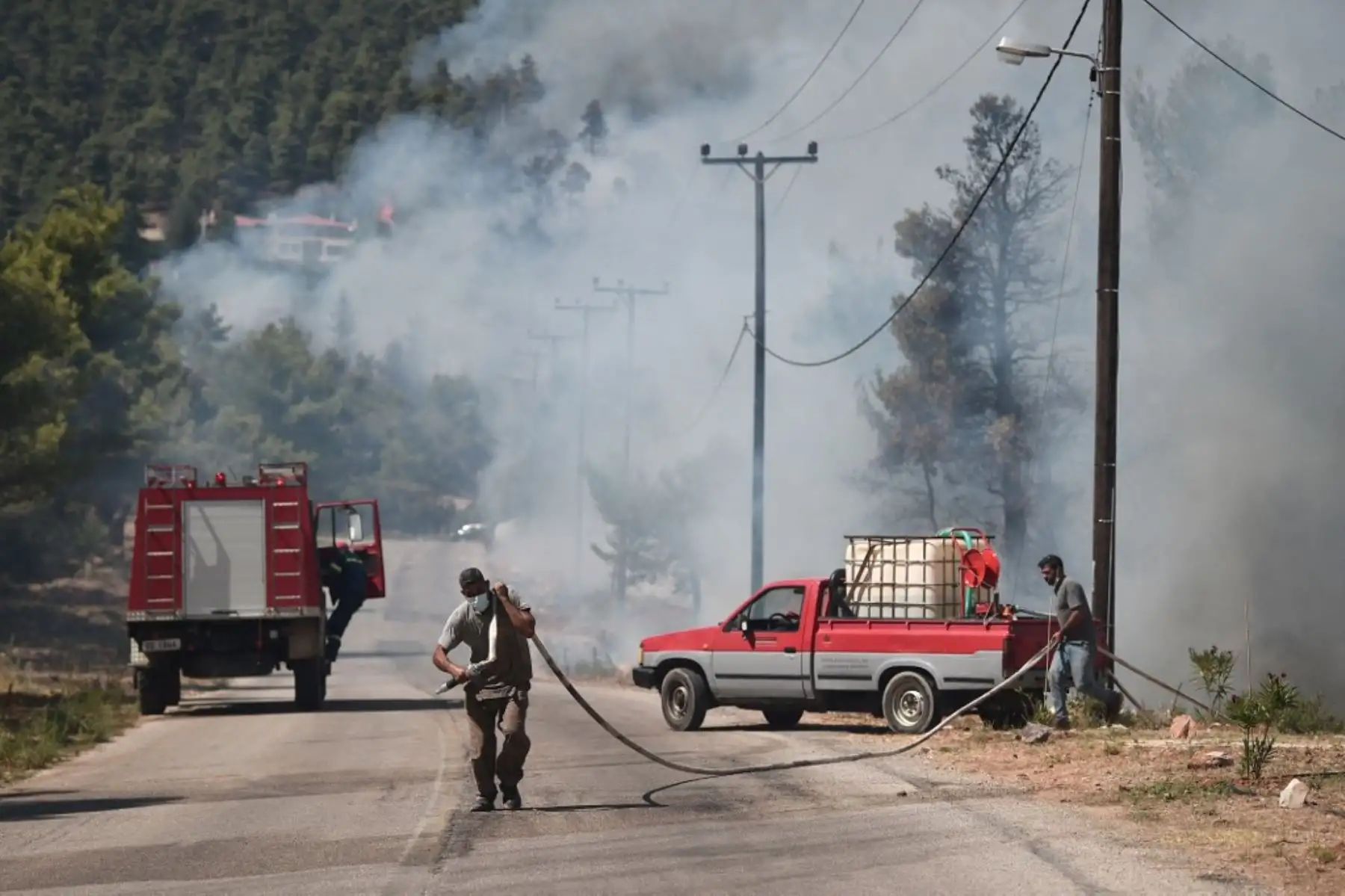 Los residentes locales llevan una tubería mientras un incendio se propaga en Ippokratios Politia, a unos 30 kilómetros al norte de Atenas, el 6 de agosto de 2021. - Cientos de bomberos combatieron un incendio en las afueras de Atenas el 6 de agosto mientras decenas de incendios se desataban en Grecia. Foto: AFP