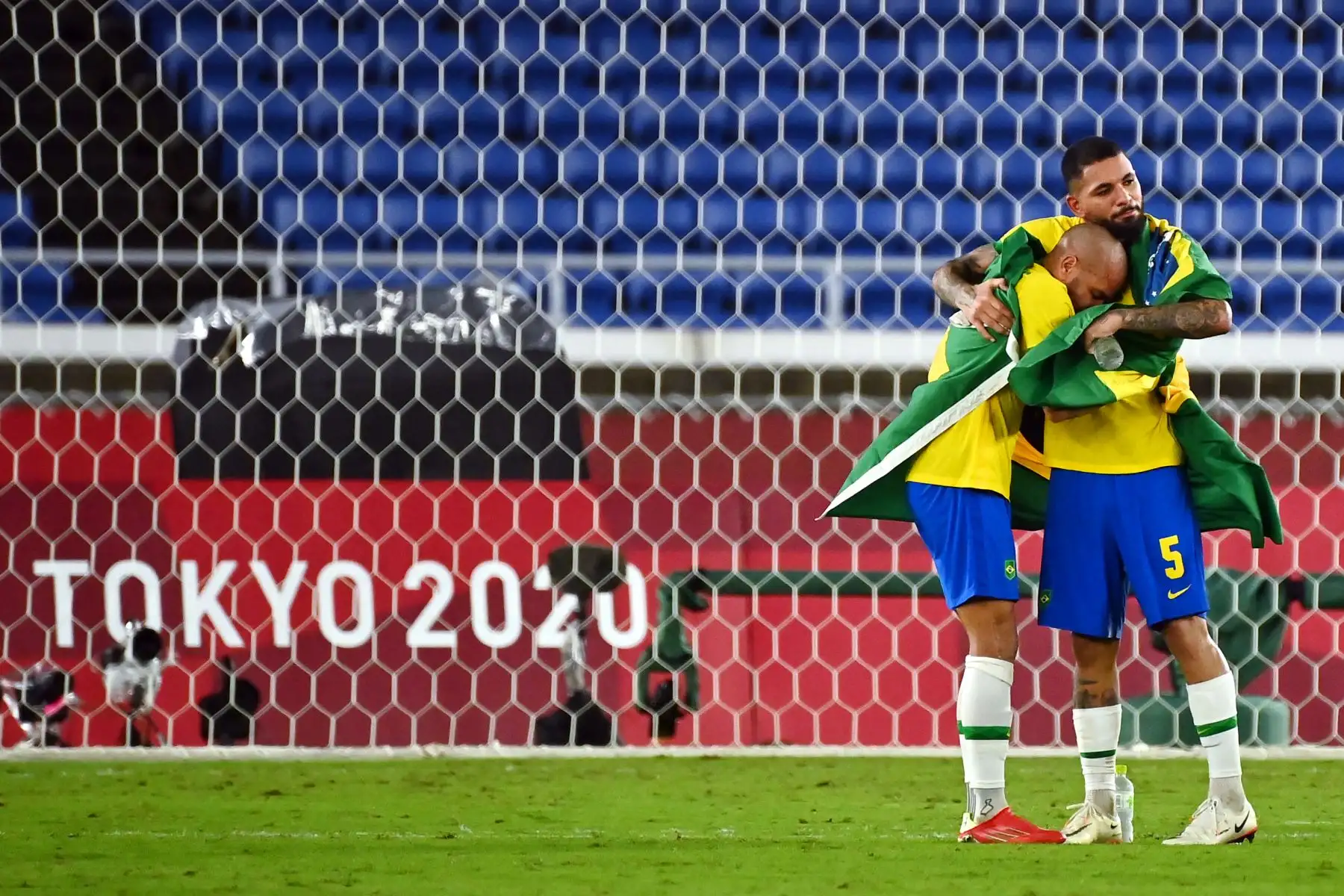 Dani Alves y Douglas Luiz envueltos en una bandera brasileña después de ganar el partido por la medalla de oro masculina de la competencia de fútbol de los Juegos Olímpicos de Tokio, en el Estadio Internacional de Yokohama. Foto: AFP