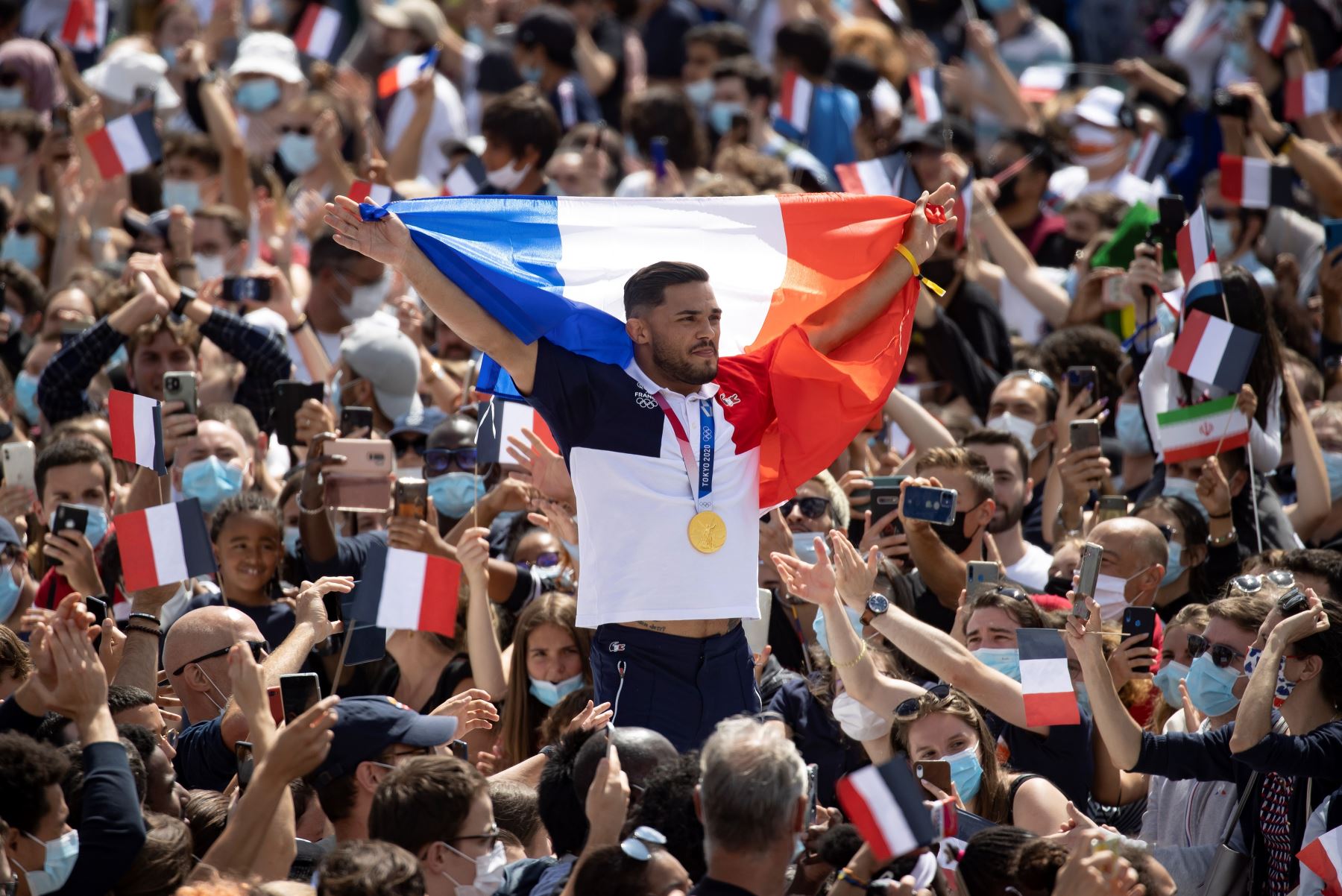 El nadador olímpico francés Florent Manaudou está rodeado por una multitud que agita banderas francesas mientras se reúnen frente a la Torre Eiffel antes de la transmisión de la ceremonia de traspaso olímpico de Tokio 2020 a París 2024. Foto: EFE