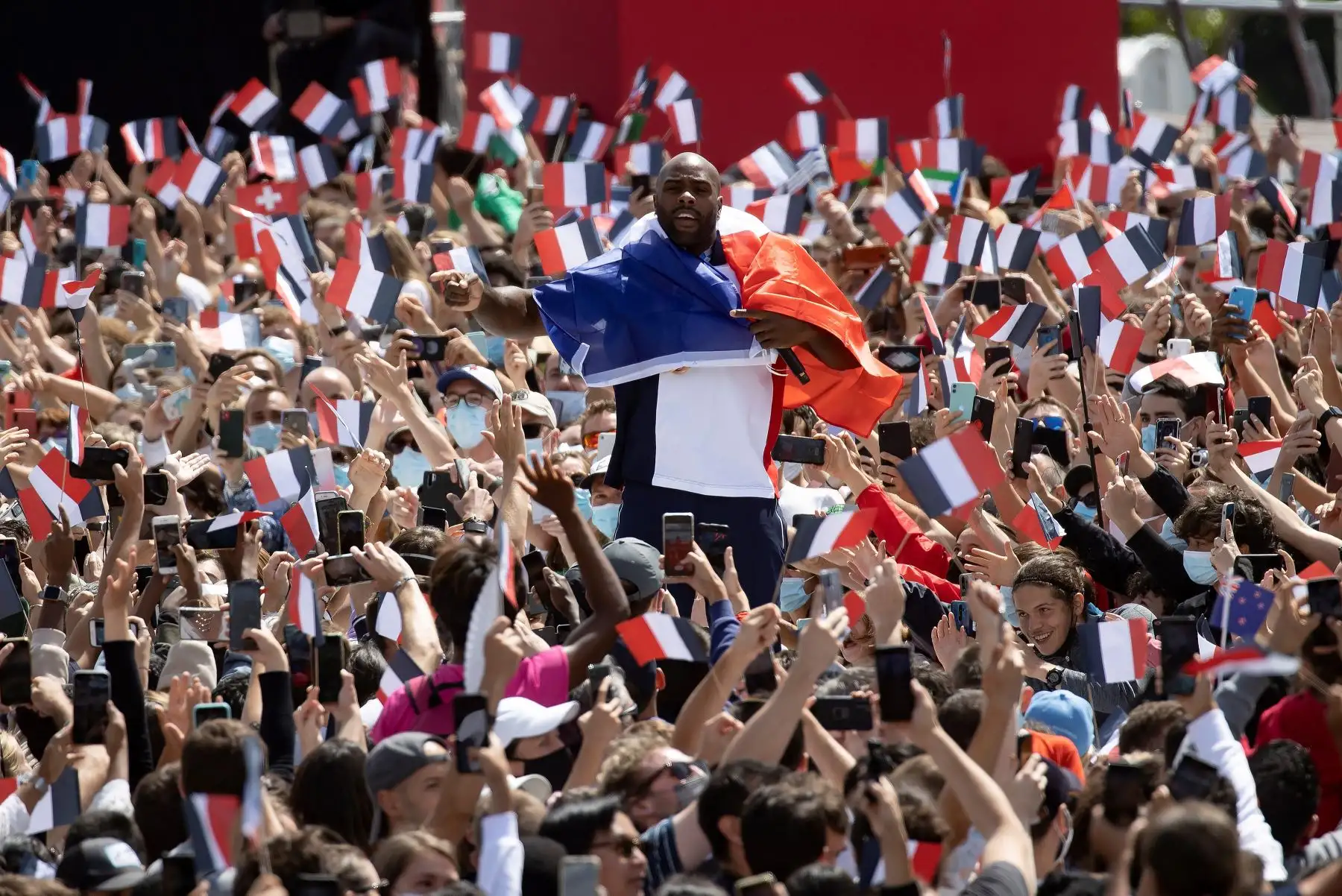 El medallista francés olímpico de judo, Teddy Riner, rodeado por una multitud que agita banderas mientras se reúnen frente a la Torre Eiffel antes de la transmisión de la ceremonia de entrega olímpica entre los Juegos Olímpicos de Tokio a París 2024. Foto: EFE