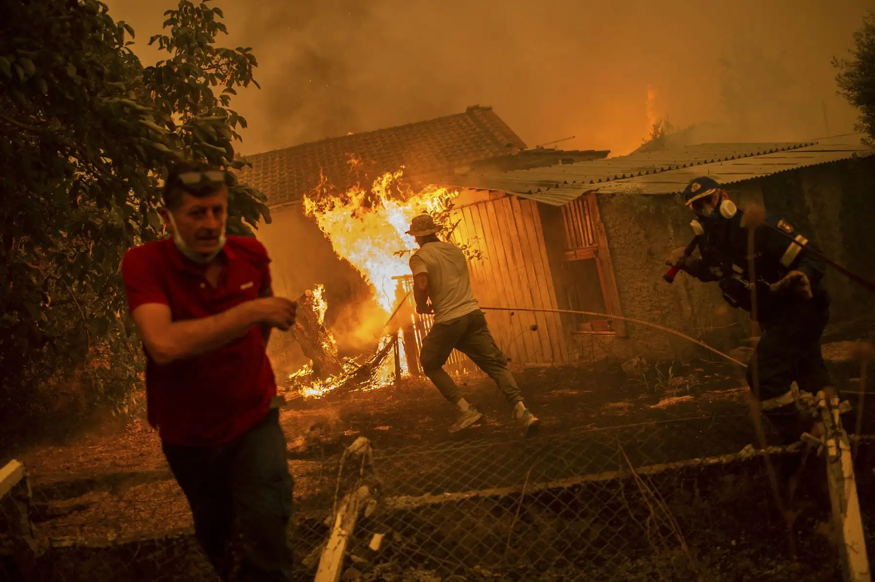 Un bombero y lugareños se apresuran para tratar de apagar las llamas de una vivienda afectada por los incendios forestales que se acercan al pueblo de Pefki en la isla de Evia, Grecia. Foto: AFP