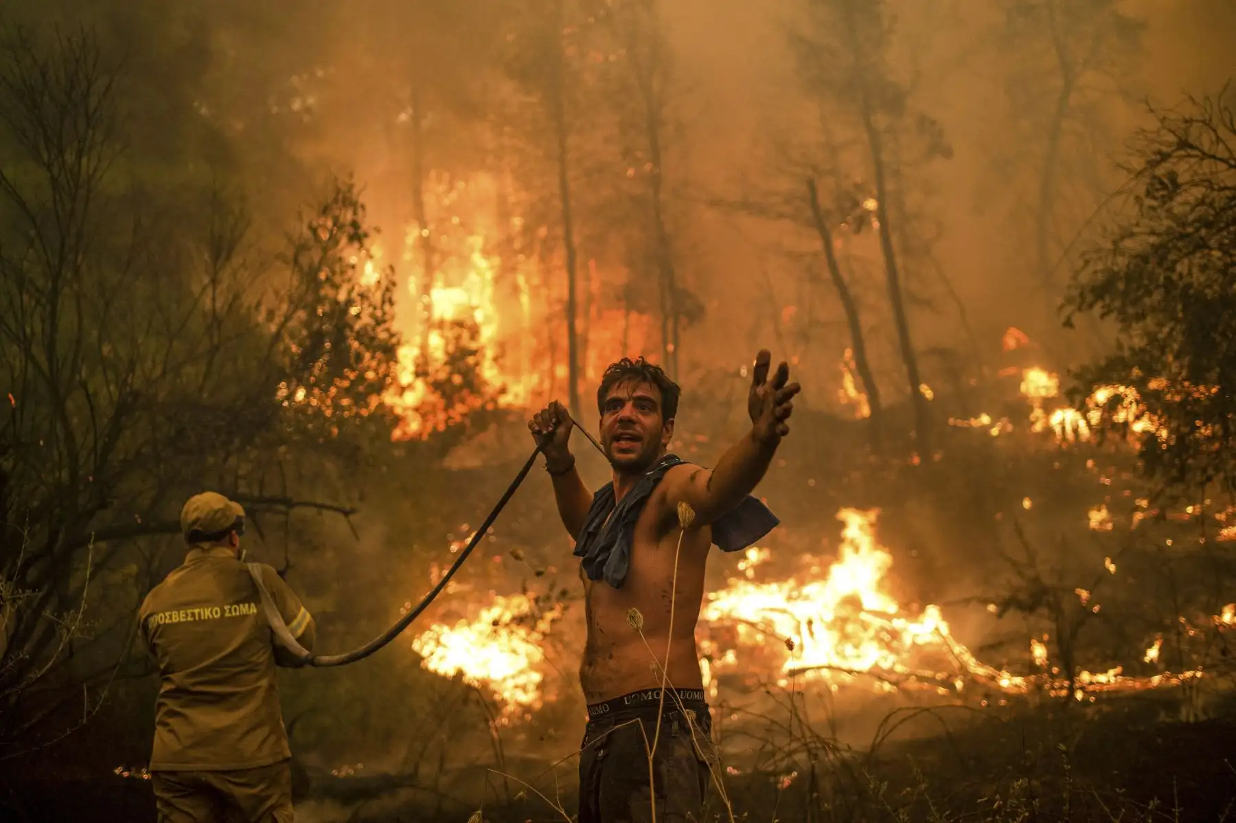 Un lugareño hace un gesto mientras sostiene una manguera de agua durante un intento de extinguir los incendios forestales que se acercan al pueblo de Pefki, en la isla de Evia, la segunda isla más grande de Grecia. Foto: AFP
