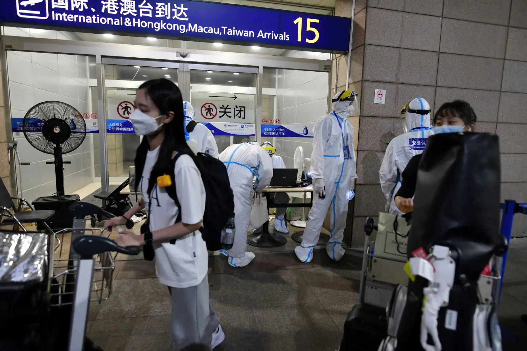 Trabajadores con ropa protectora como precaución contra el covid-19 ayudan a los pasajeros internacionales que llegan mientras se preparan para abordar los autobuses que los llevarán a los hoteles de cuarentena, en el aeropuerto de Pudong en Shanghai.
Foto: AFP