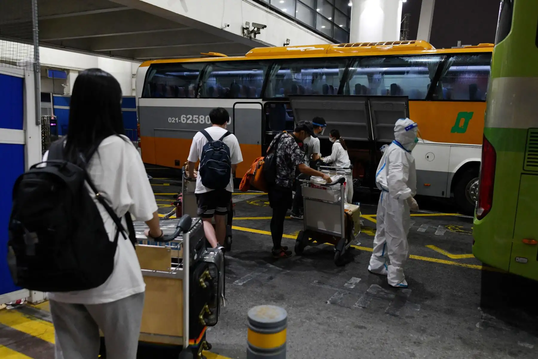 Trabajadores con ropa protectora como precaución contra el coronavirus  ayudan a los pasajeros internacionales que llegan mientras se preparan para abordar los autobuses que los llevarán a los hoteles de cuarentena, en el aeropuerto de Pudong en Shanghai.
Foto: AFP