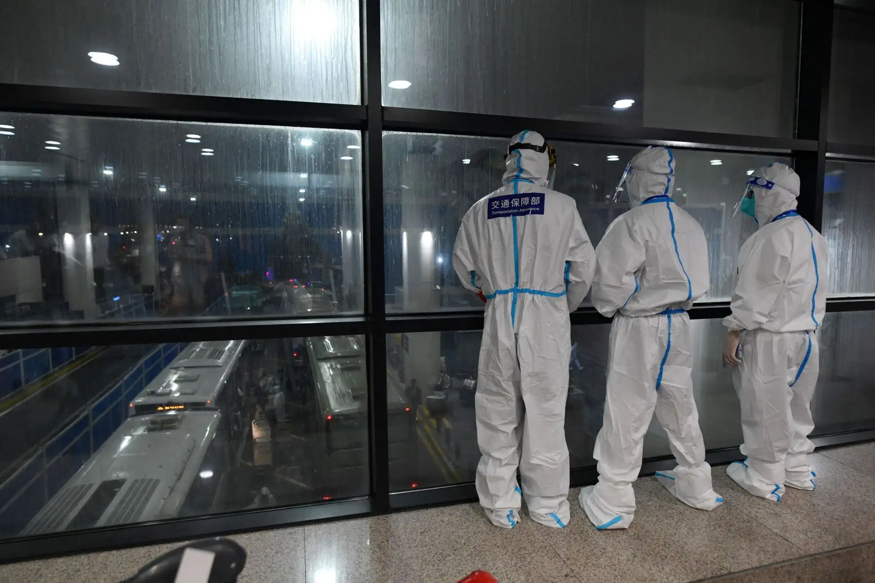 Trabajadores con ropa protectora como precaución contra el coronavirus  vigilan a los internacionales pasajeros que llegan mientras suben a los autobuses para ser llevados a hoteles en cuarentena, en el aeropuerto de Pudong en Shanghai.
Foto: AFP