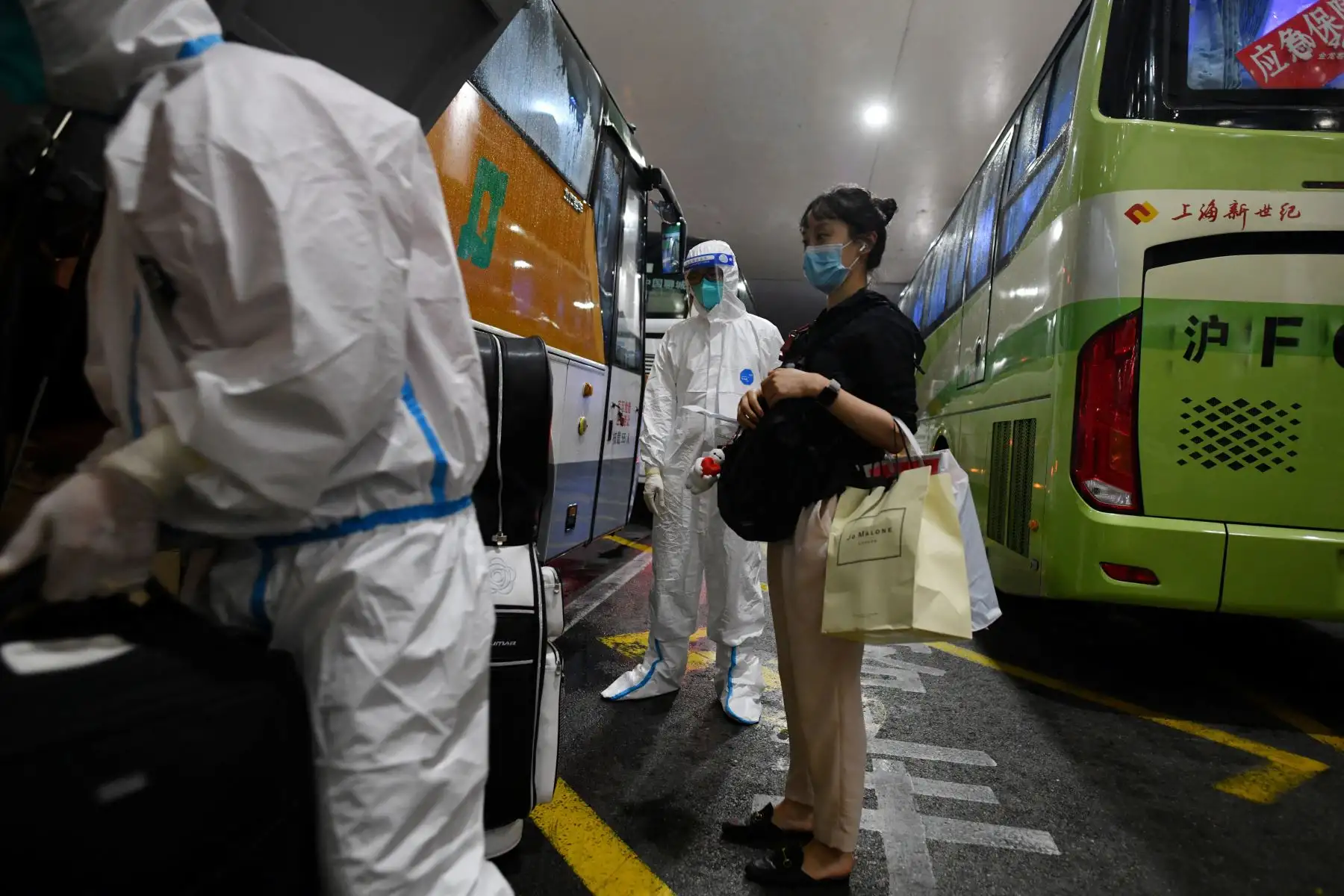 Trabajadores con ropa protectora como precaución contra el covid-19 ayudan a los pasajeros internacionales que llegan mientras se preparan para abordar los autobuses que los llevarán a los hoteles de cuarentena, en el aeropuerto de Pudong en Shanghai.
Foto: AFP